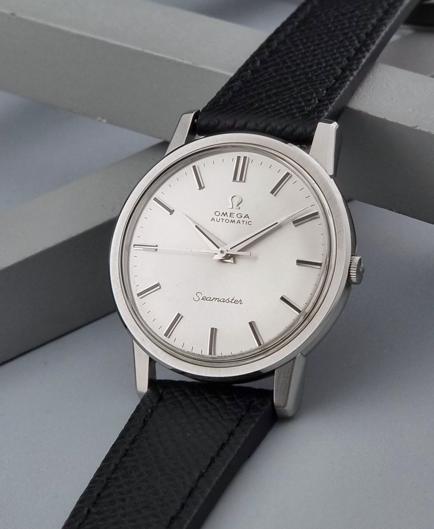 Vintage Omega Wristwatch Seamaster 165.003 with a silver-toned round case and black textured strap, shown on a gray background crown view