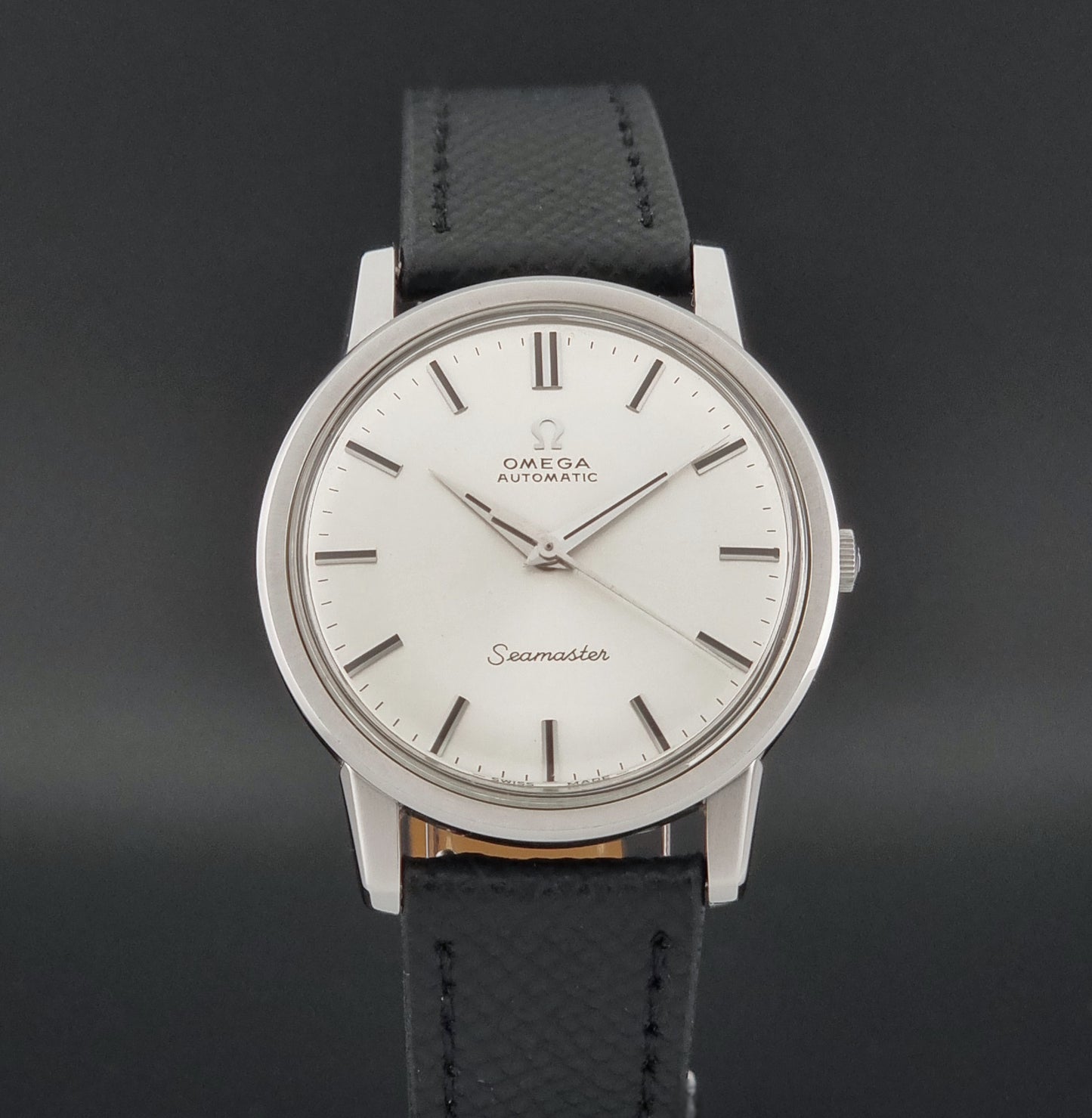 Vintage Omega Wristwatch Seamaster 165.003 with a silver-toned round case and black textured strap, shown on a gray background close dial view