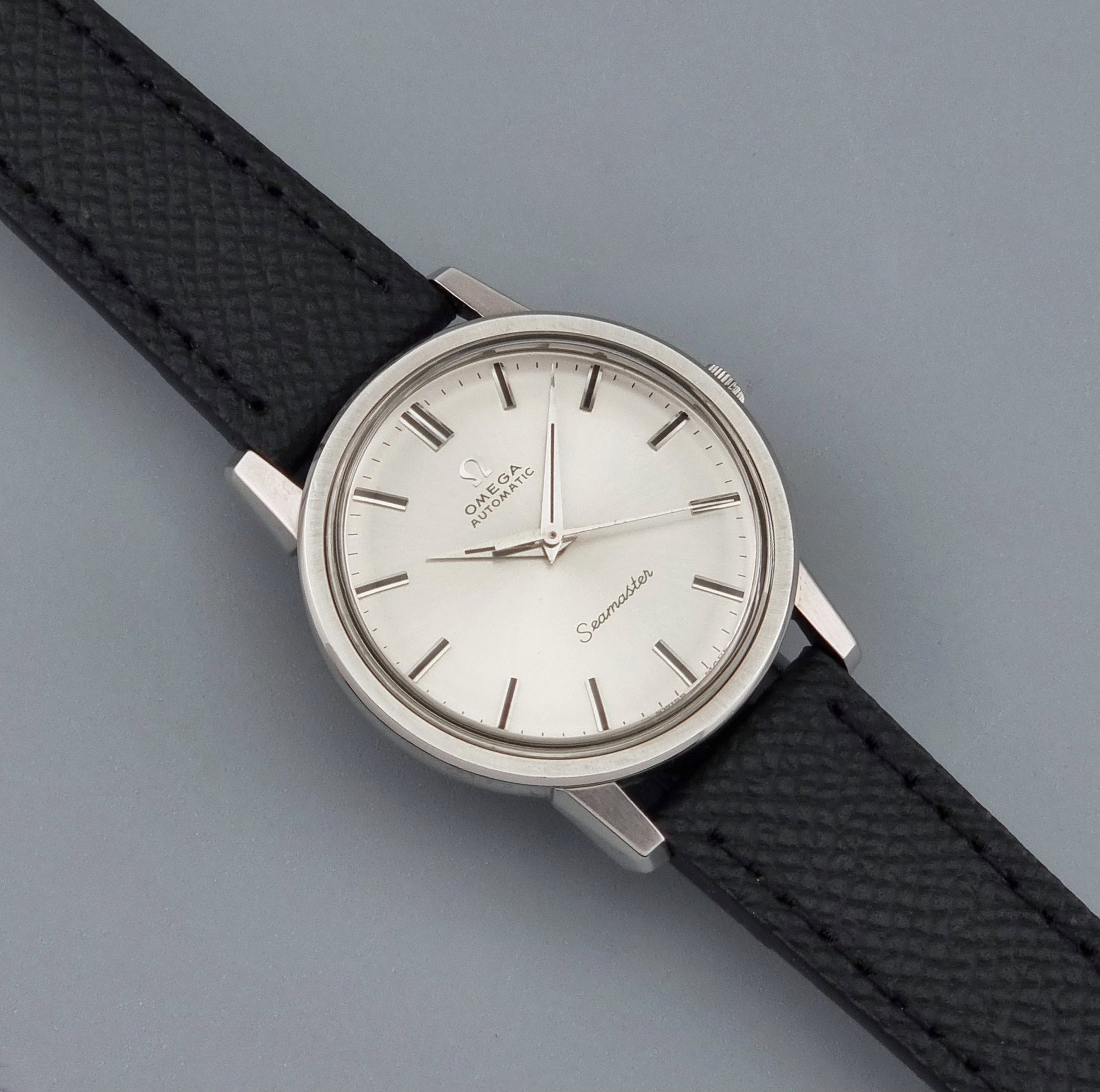 Vintage Omega Wristwatch Seamaster 165.003 with a silver-toned round case and black textured strap, shown on a gray background dial