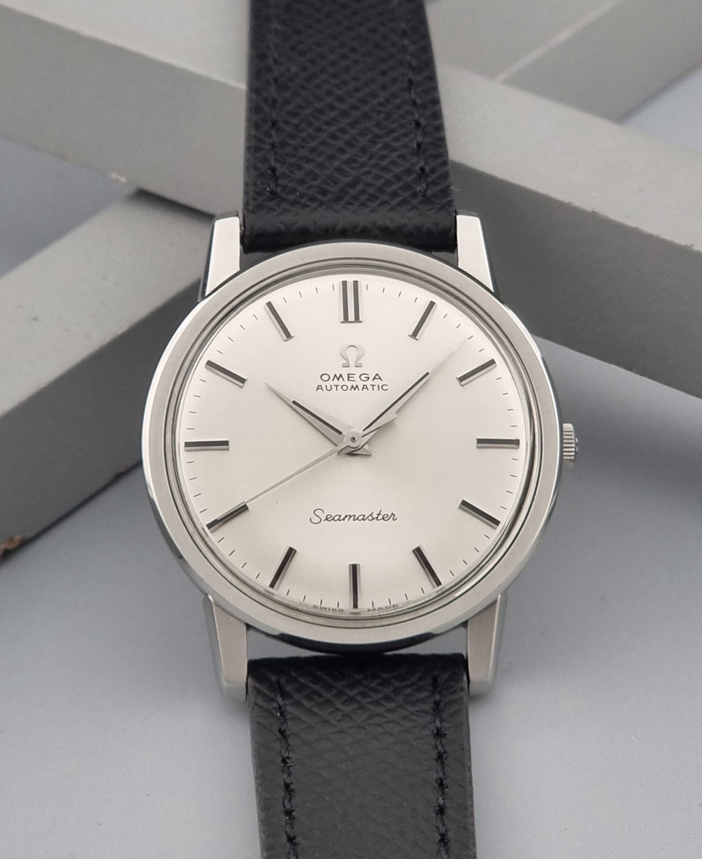 Vintage Omega Wristwatch Seamaster 165.003 with a silver-toned round case and black textured strap, shown on a gray background dial view