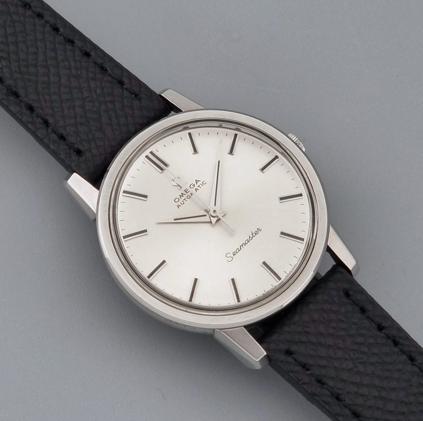 Vintage Omega Wristwatch Seamaster 165.003 with a silver-toned round case and black textured strap, shown on a gray background close up dial view