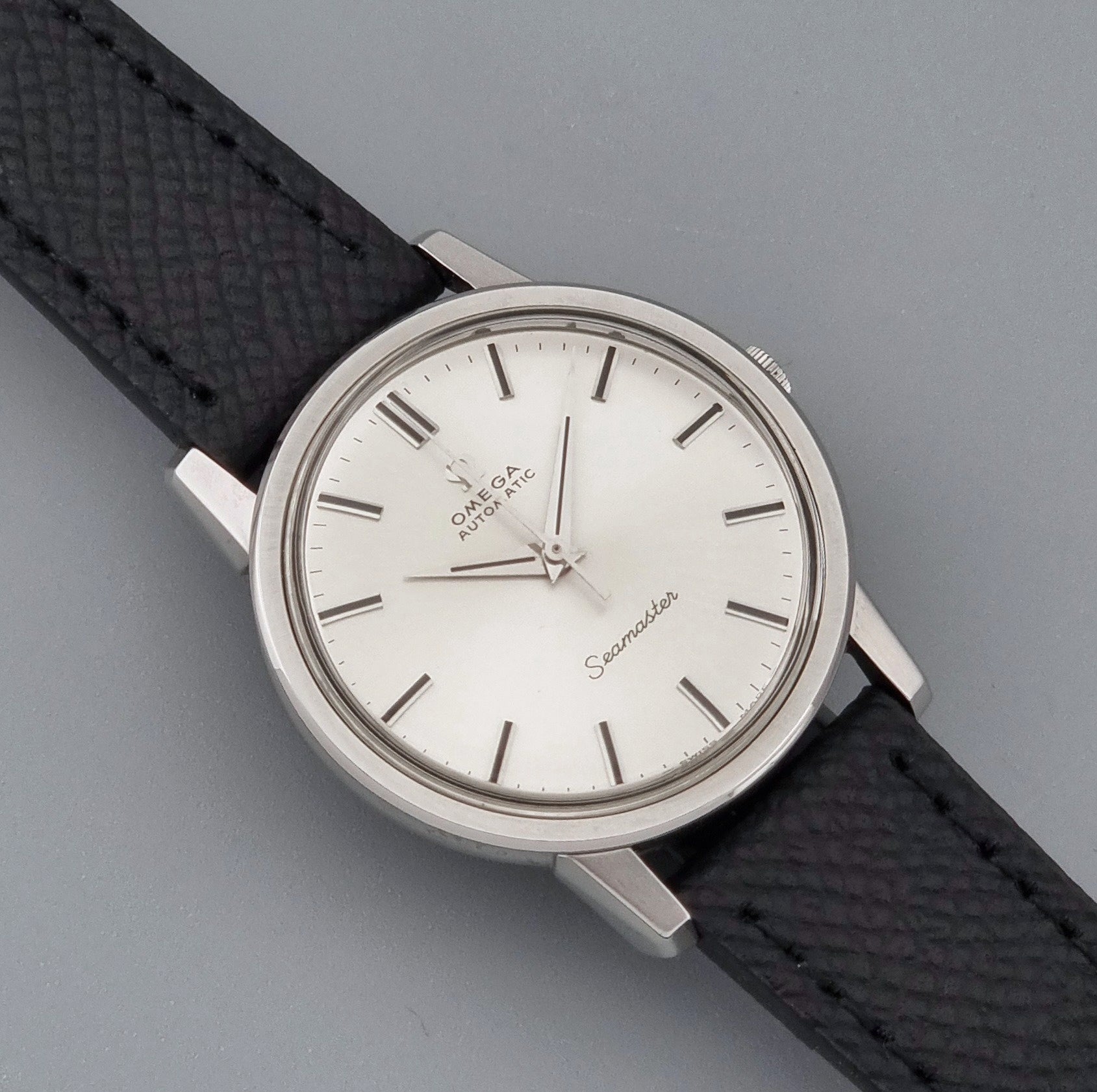 Vintage Omega Wristwatch Seamaster 165.003 with a silver-toned round case and black textured strap, shown on a gray background close up dial view