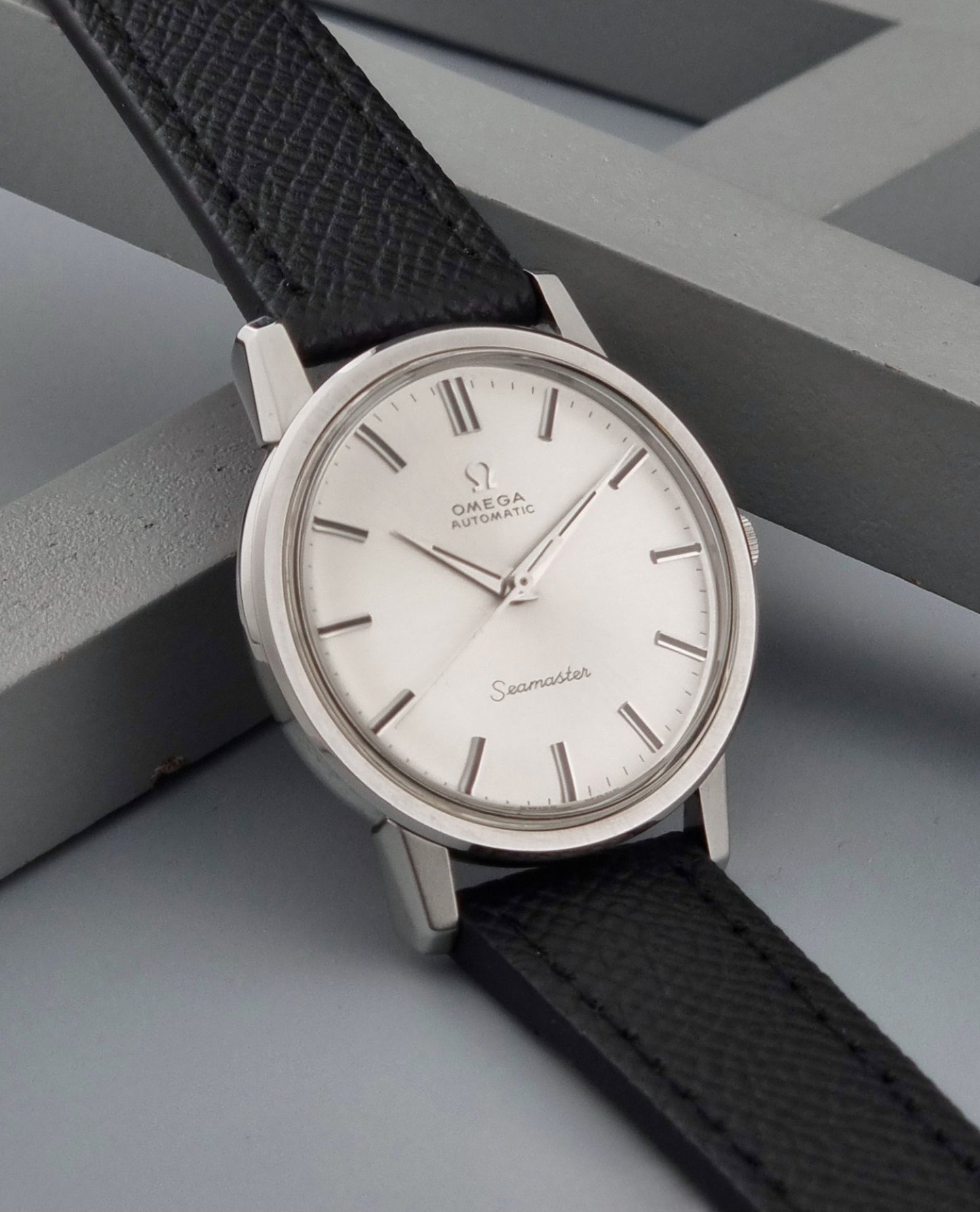 Vintage Omega Wristwatch Seamaster 165.003 with a silver-toned round case and black textured strap, shown on a gray background side view