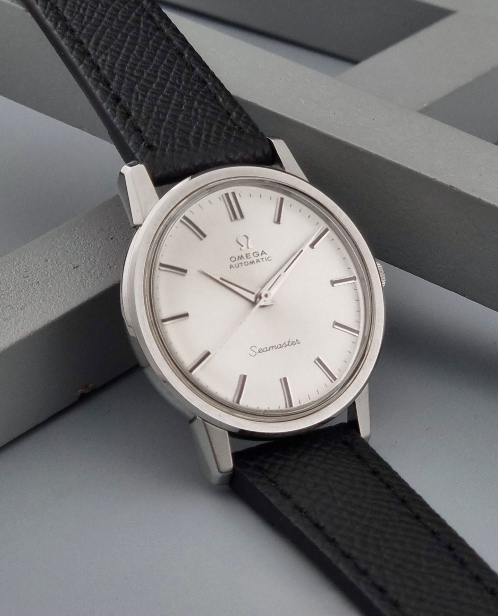Vintage Omega Wristwatch Seamaster 165.003 with a silver-toned round case and black textured strap, shown on a gray background side view