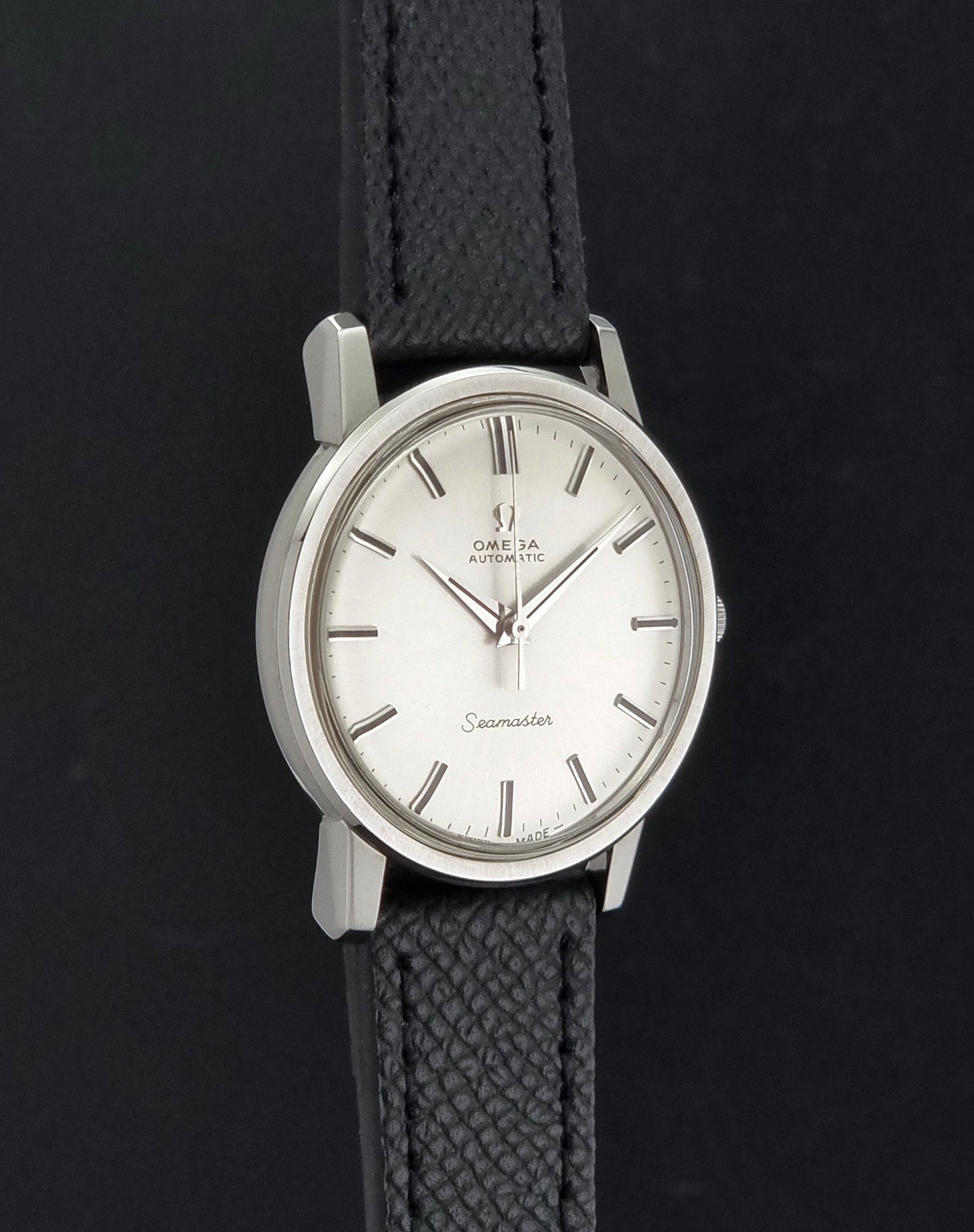 Vintage Omega Wristwatch Seamaster 165.003 with a silver-toned round case and black textured strap, shown on a gray background side profile view