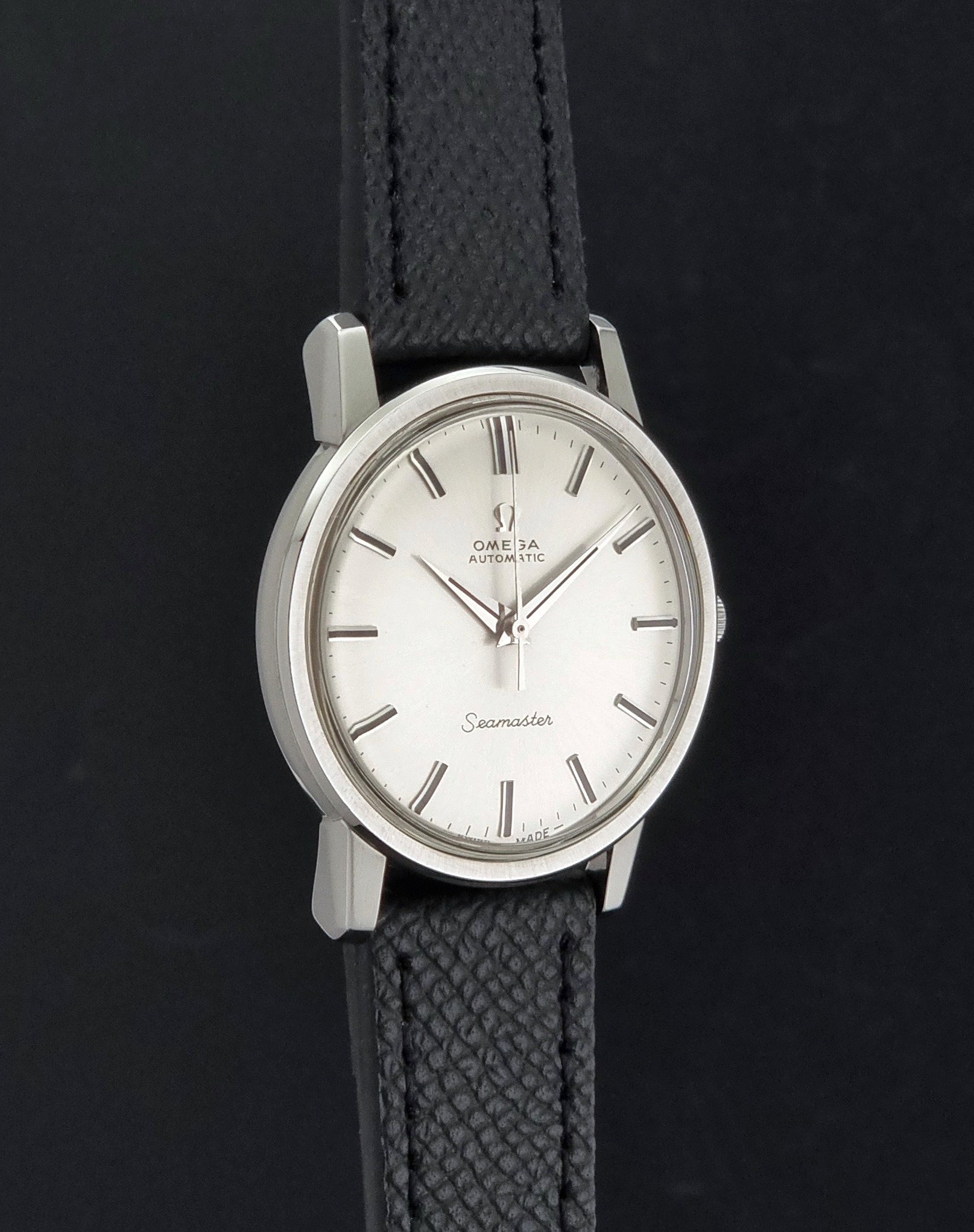 Vintage Omega Wristwatch Seamaster 165.003 with a silver-toned round case and black textured strap, shown on a gray background side profile view