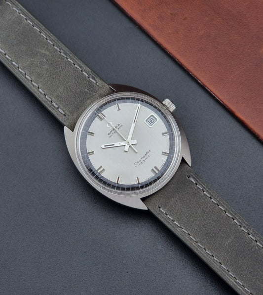 Vintage Omega Wristwatch 166.026 Seamaster Cosmic with gray leather strap on a dark surface dial up