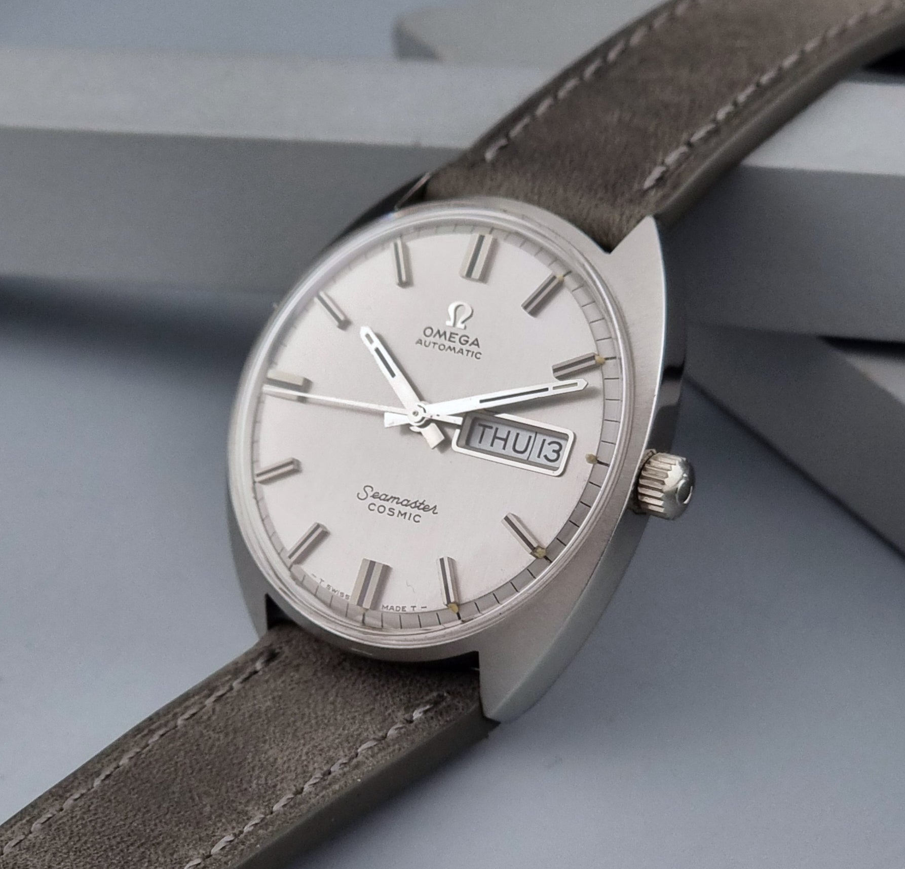 Vintage Omega Wristwatch Seamaster Cosmic 166.036 with a grey leather strap on a gray background crown side view