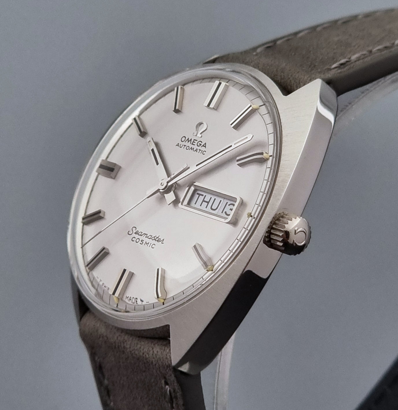 Vintage Omega Wristwatch Seamaster Cosmic 166.036 with a grey leather strap on a gray background crown profile view