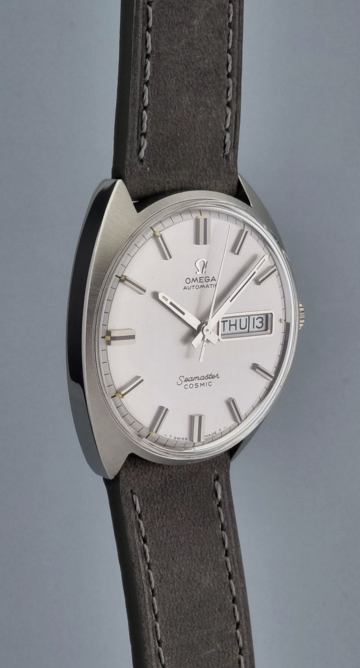 Vintage Omega Wristwatch Seamaster Cosmic 166.036 with a grey leather strap on a gray background side profile