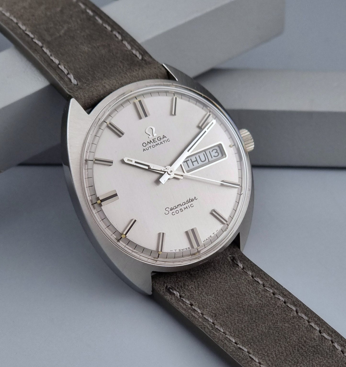 Vintage Omega Wristwatch Seamaster Cosmic 166.036 with a grey leather strap on a gray background side view