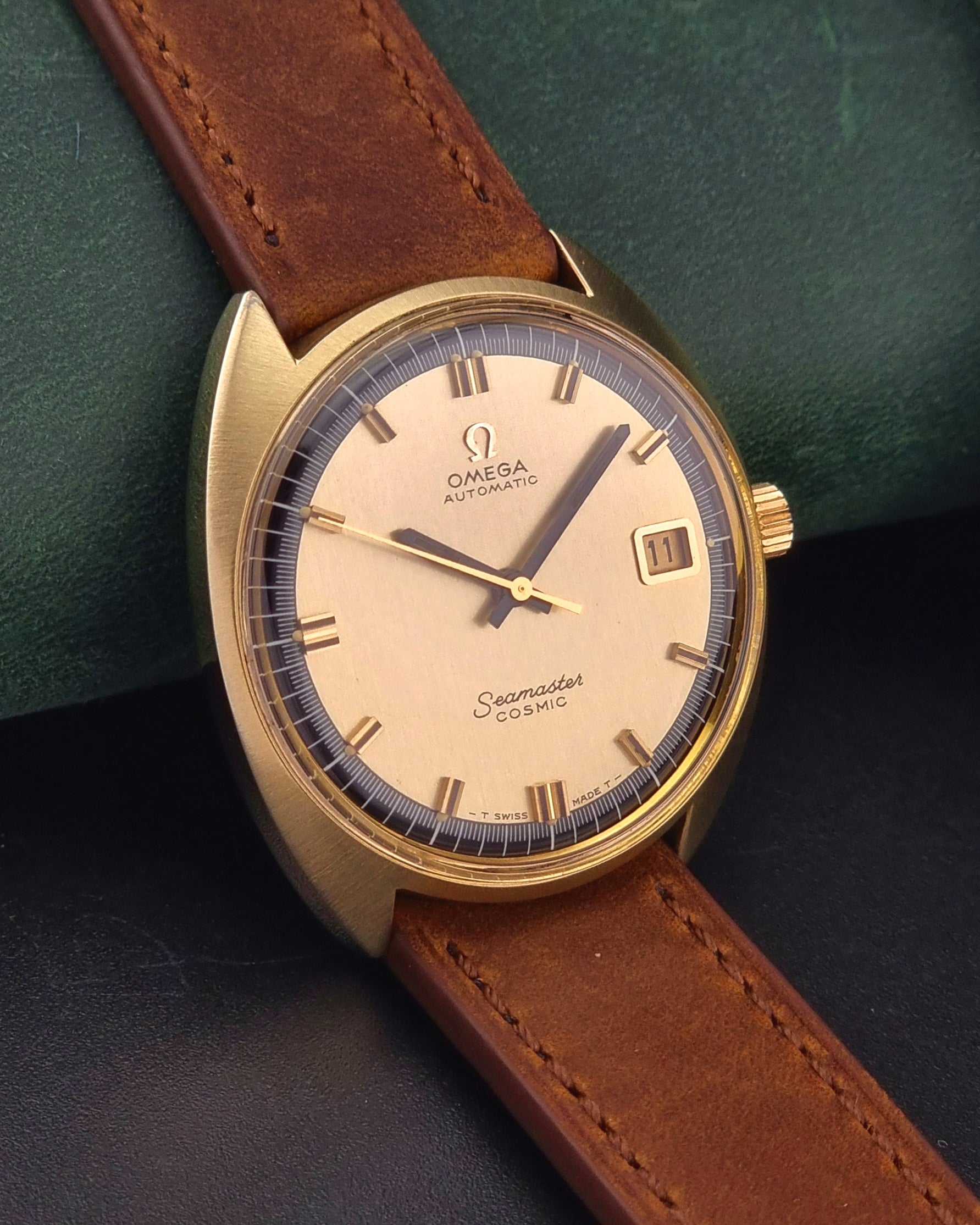 Gold Omega watch with brown leather strap on a dark green background