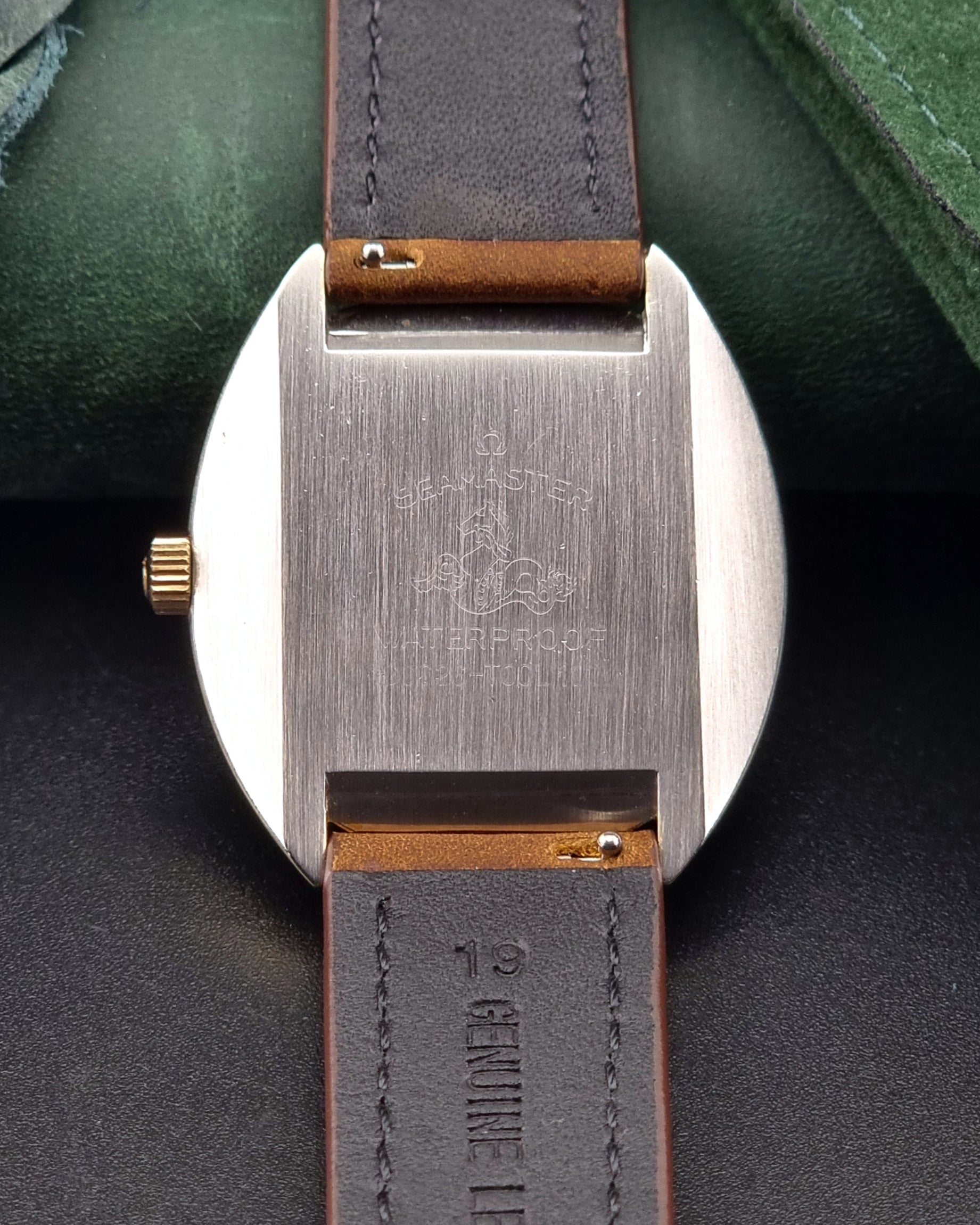 Close-up of an Omega watch caseback with a brown leather strap on a dark background