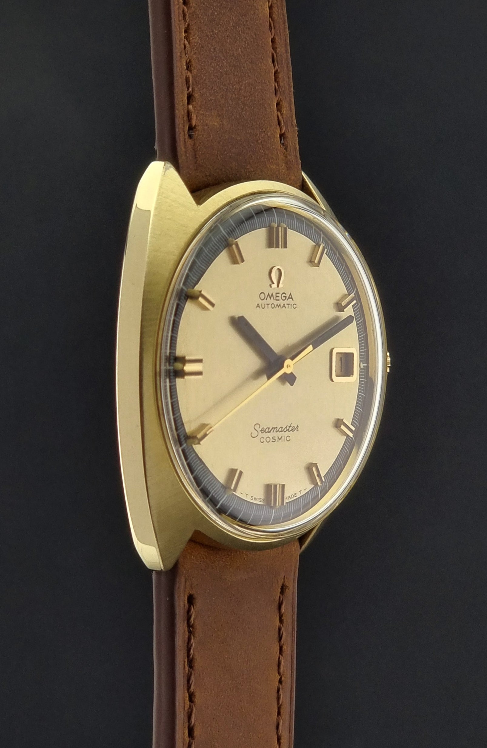 Vintage Omega watch with gold case and brown leather strap on a black background