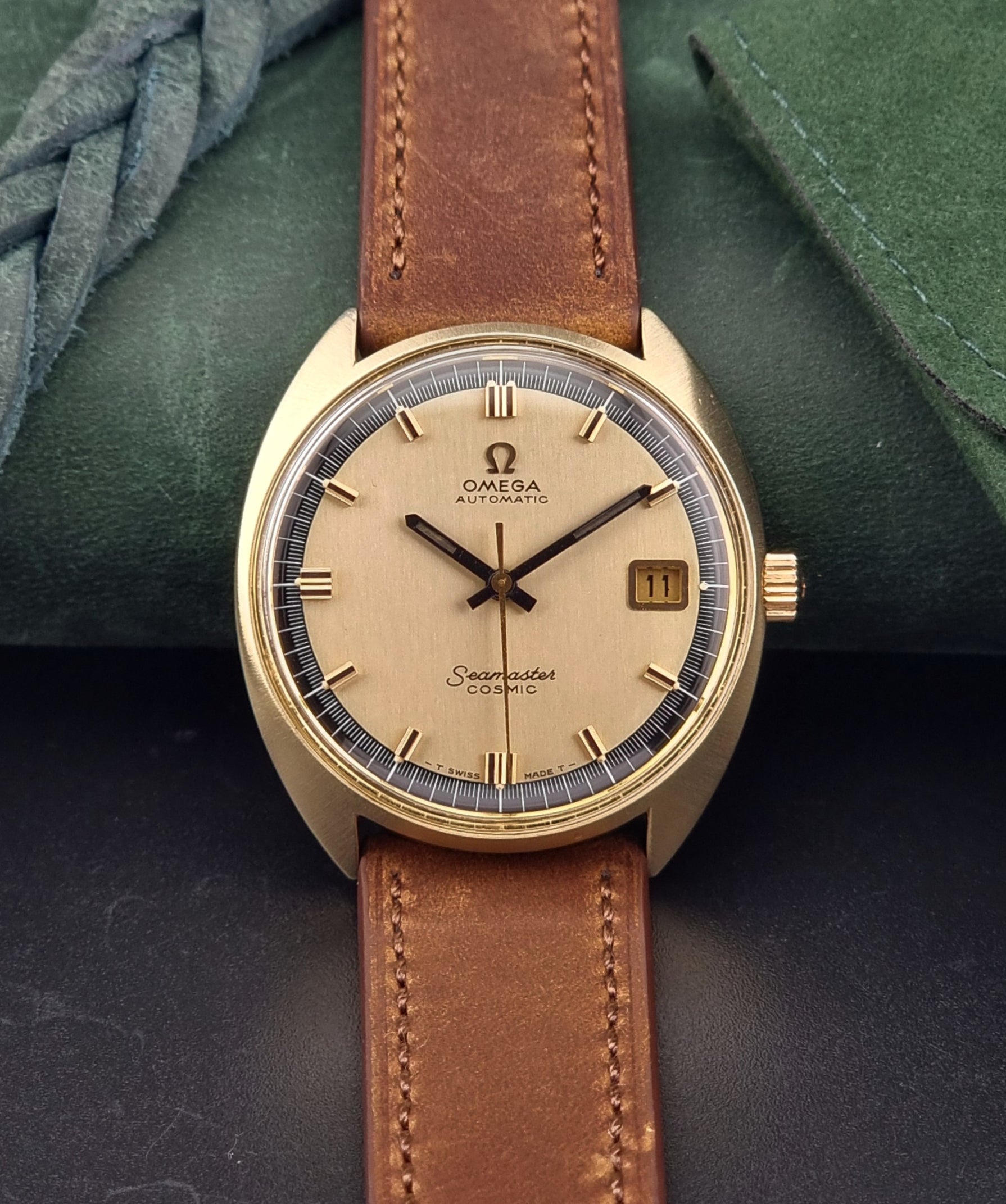 Gold Omega watch with brown leather strap on a dark surface
