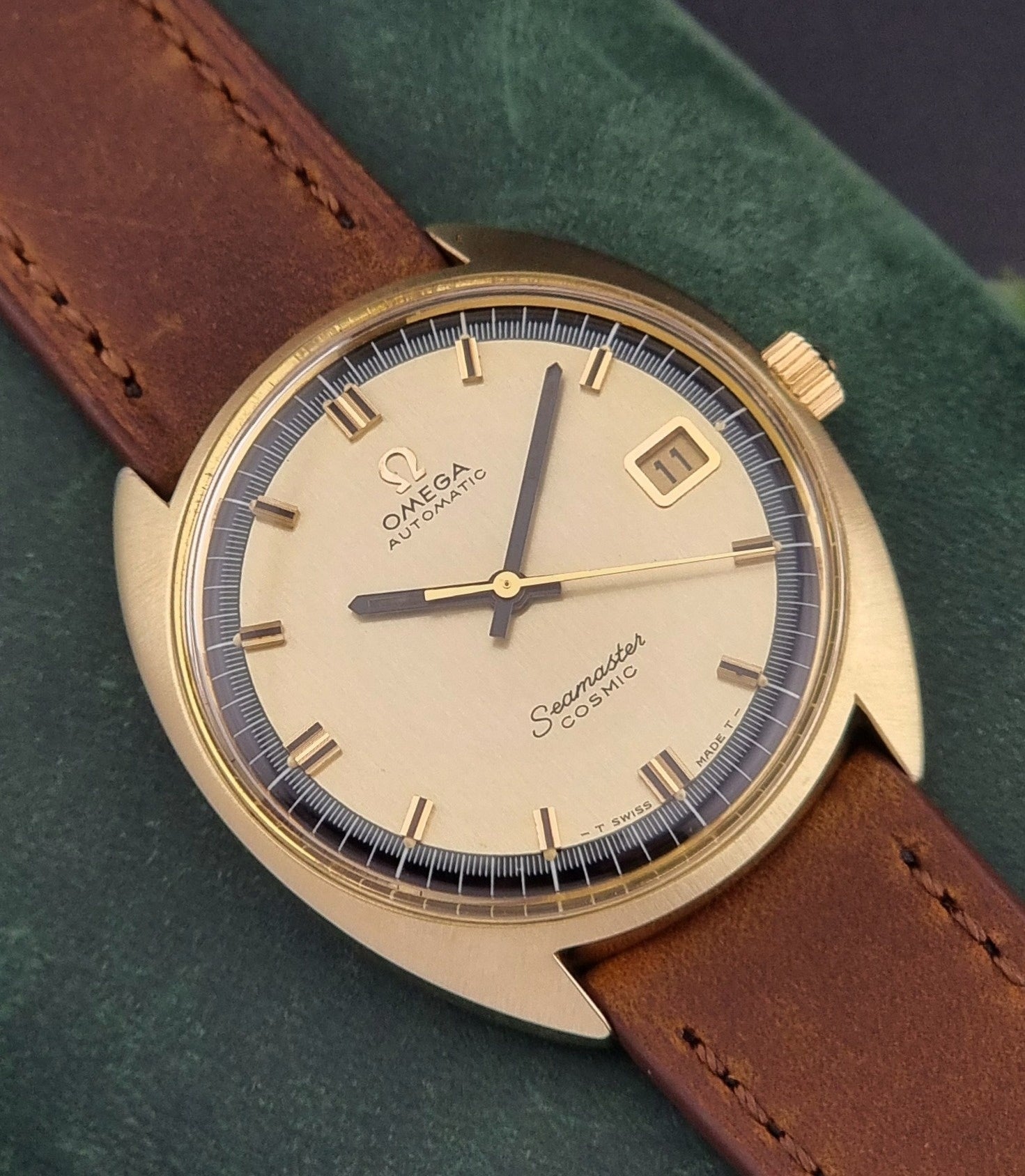 Vintage Omega watch with brown leather strap on a green background