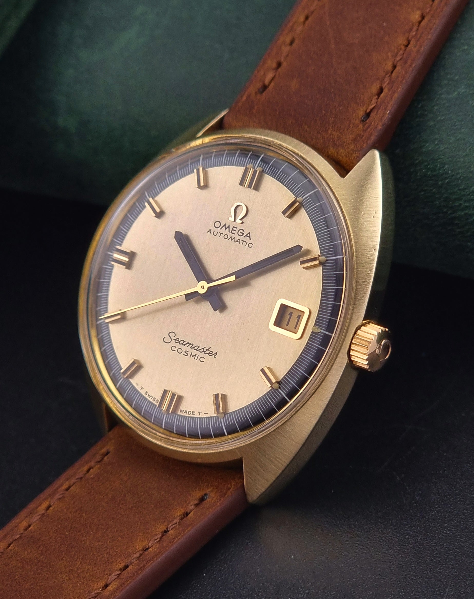 Gold Omega watch with brown leather strap on a dark background