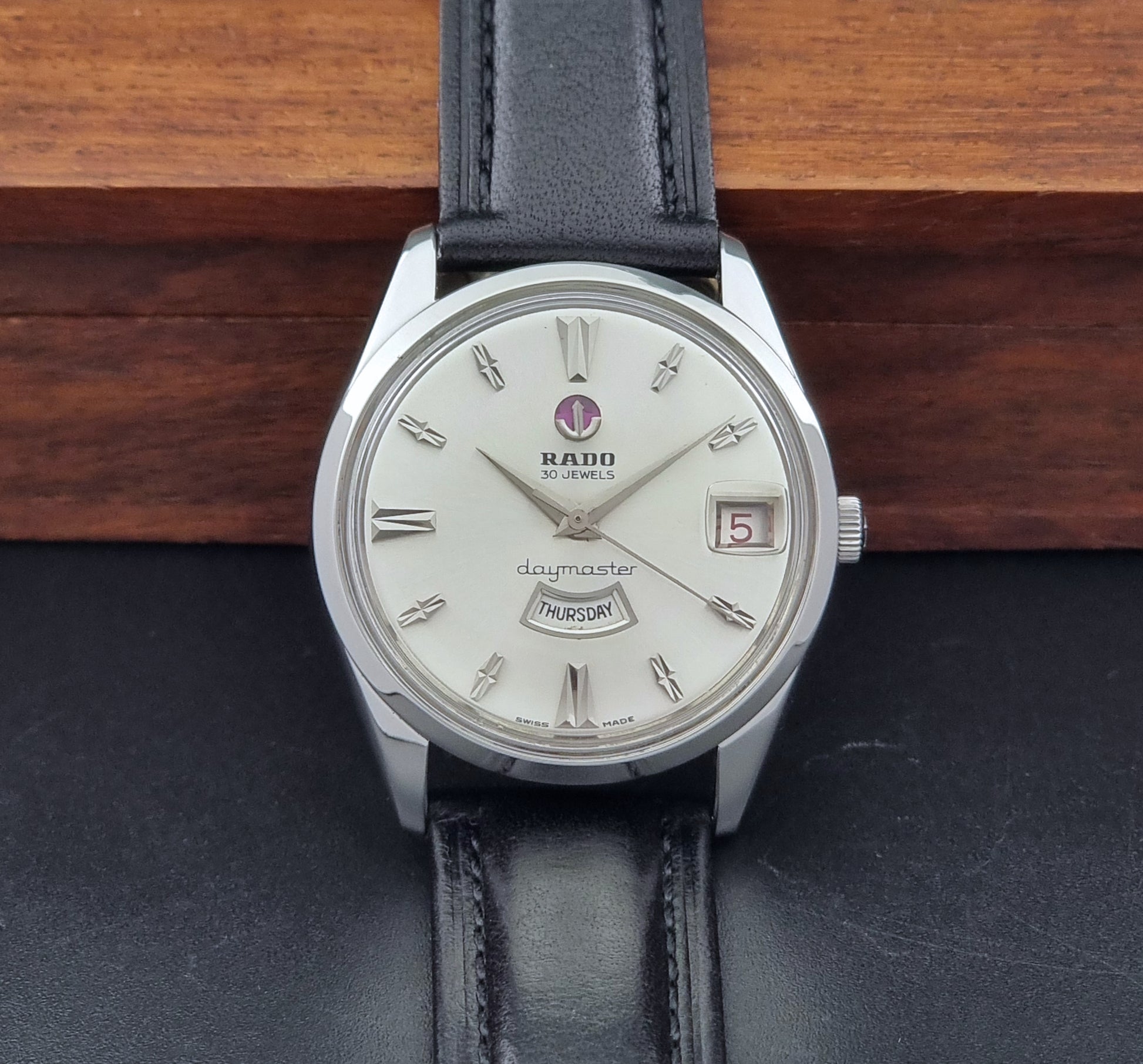 Vintage Rado wristwatch Daymaster 11754 with black leather strap on a dark surface front view