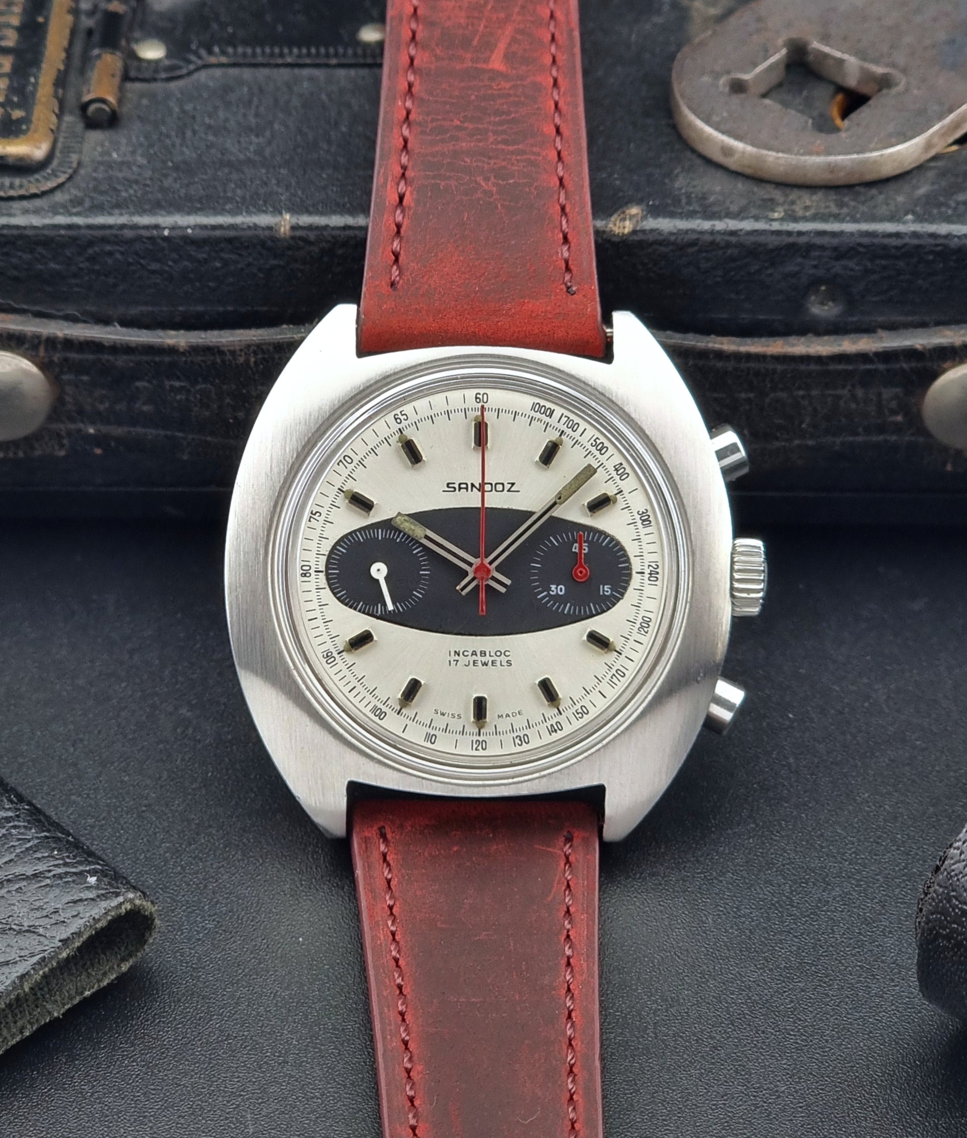 Vintage Sandoz watch with red leather strap on a dark textured surface