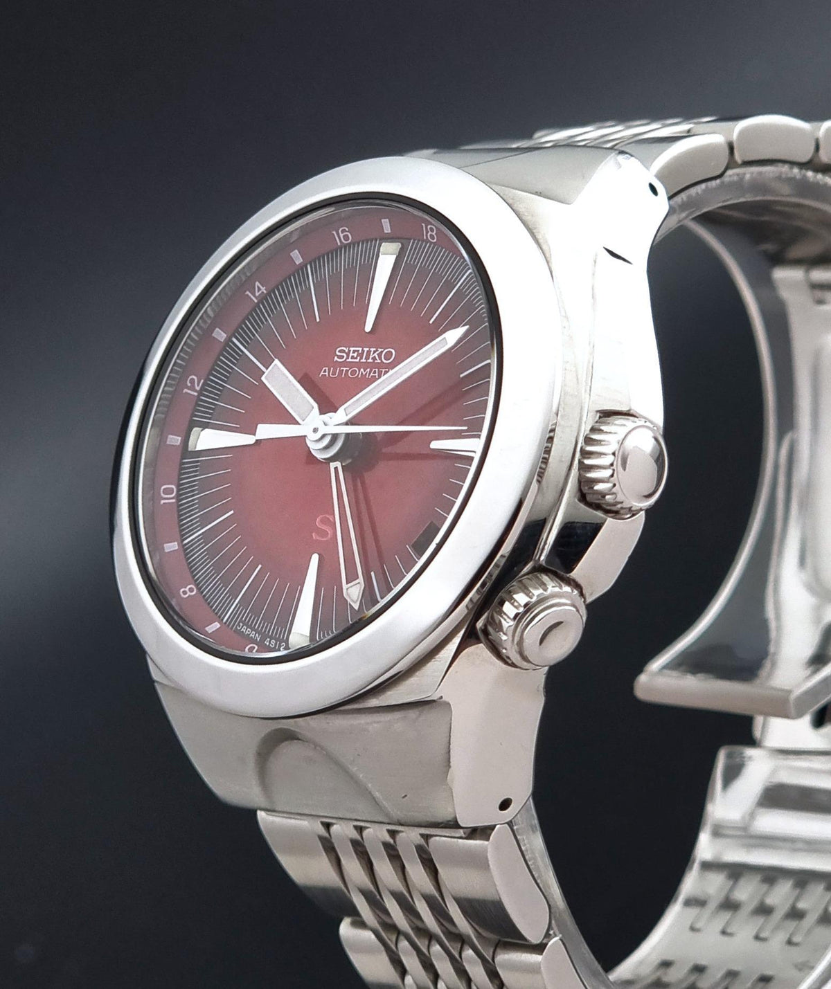 A close-up shot of a Seiko watch Mechasus SCFF007 GMT 4S12-0010 featuring a silver stainless steel case and bracelet, with a distinctive red dial and silver indices.
