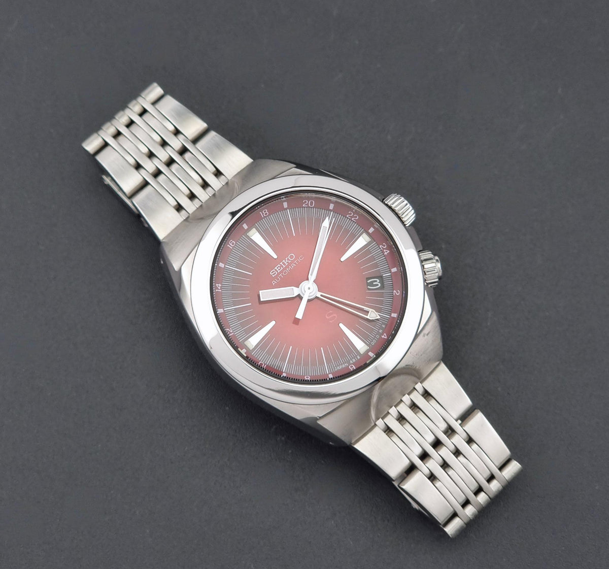 Seiko watch Mechasus SCFF007 GMT 4S12-0010 with a silver stainless steel case and multi-link bracelet, featuring a distinctive red sunburst dial with silver indices, photographed on a dark gray textured background.