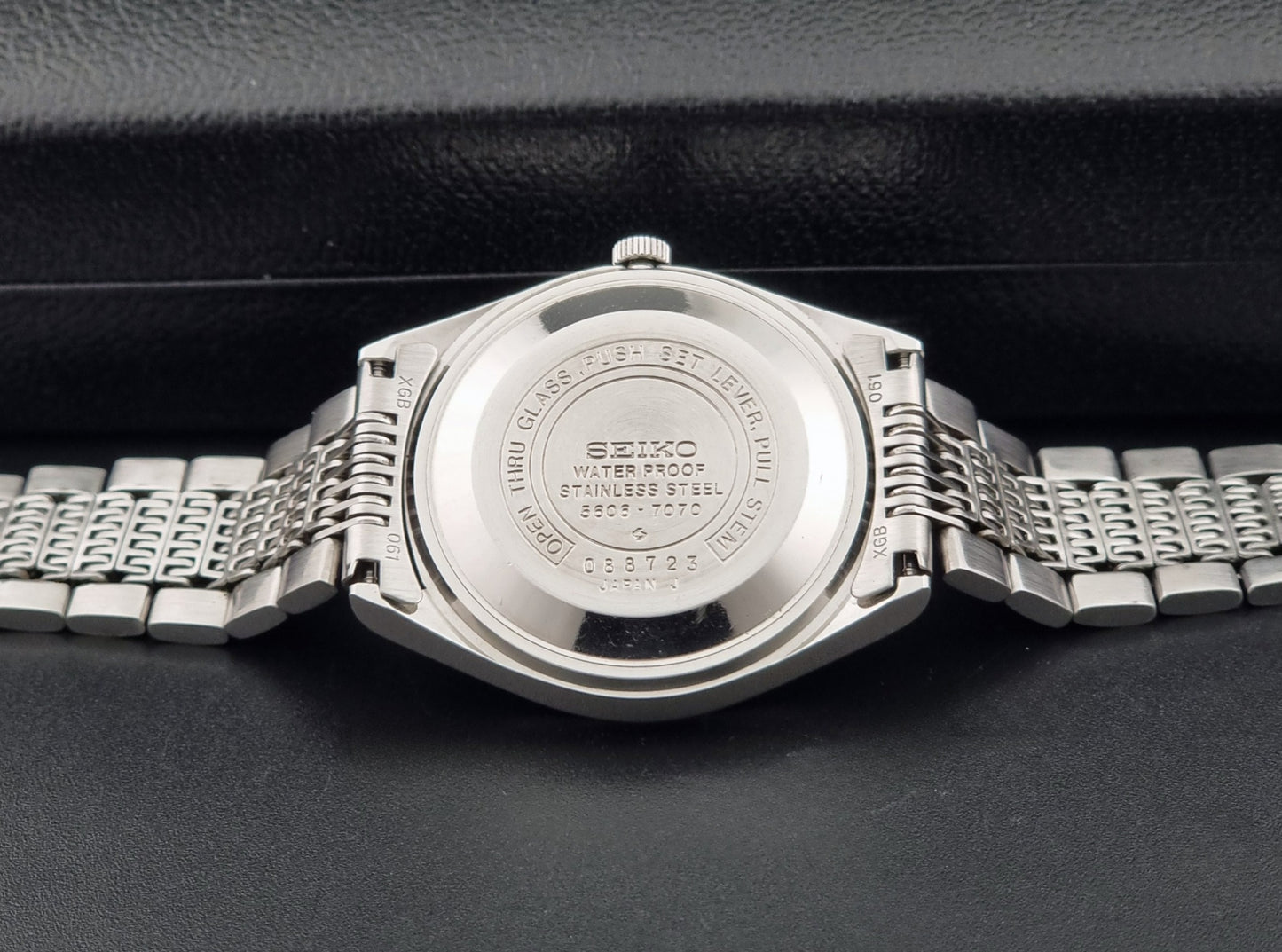 Vintage Seiko 5606-7070 LordMatic with a stainless steel bracelet on a dark background case back view