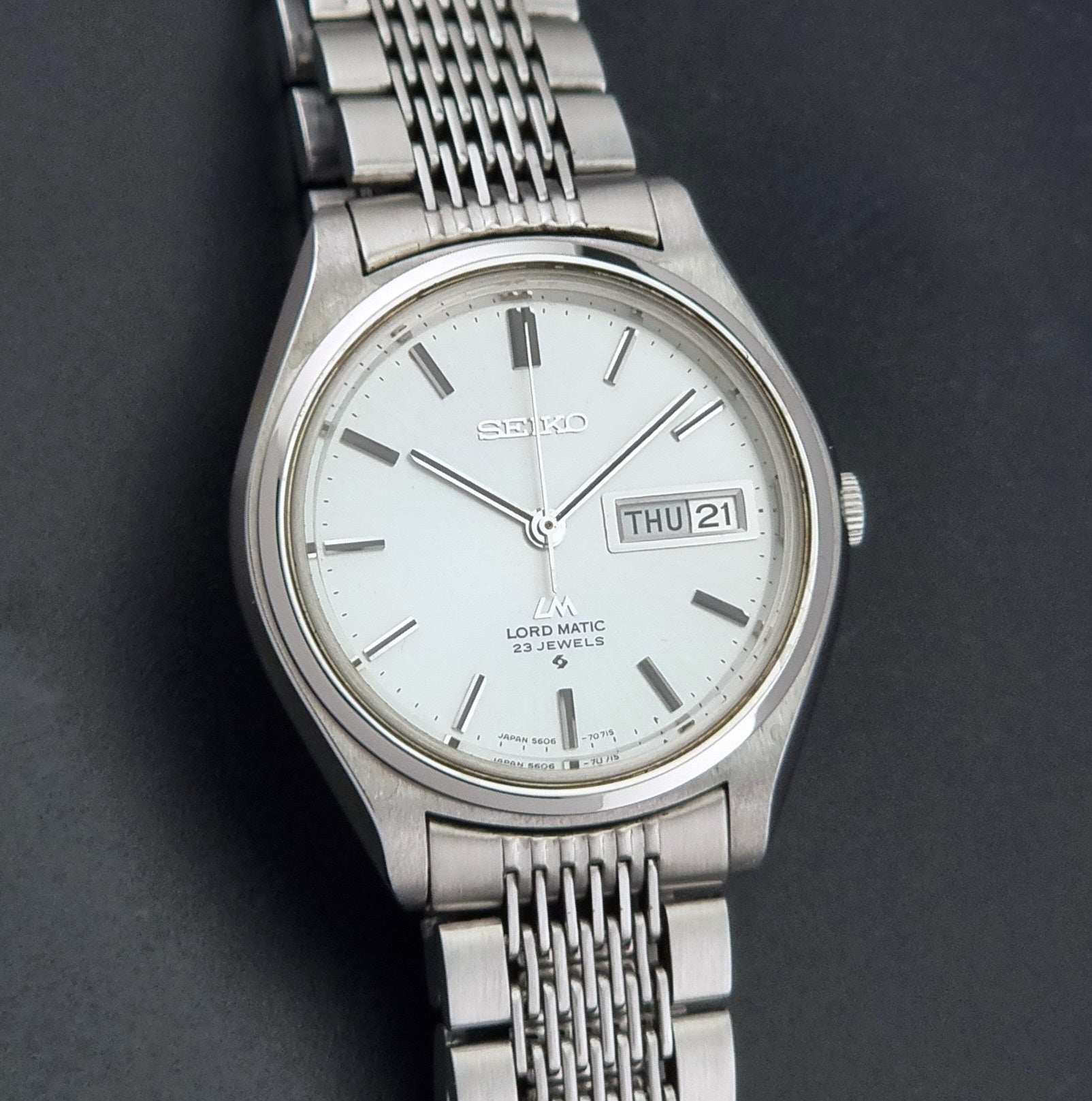 Vintage Seiko 5606-7070 LordMatic with a stainless steel bracelet on a dark background close dial view
