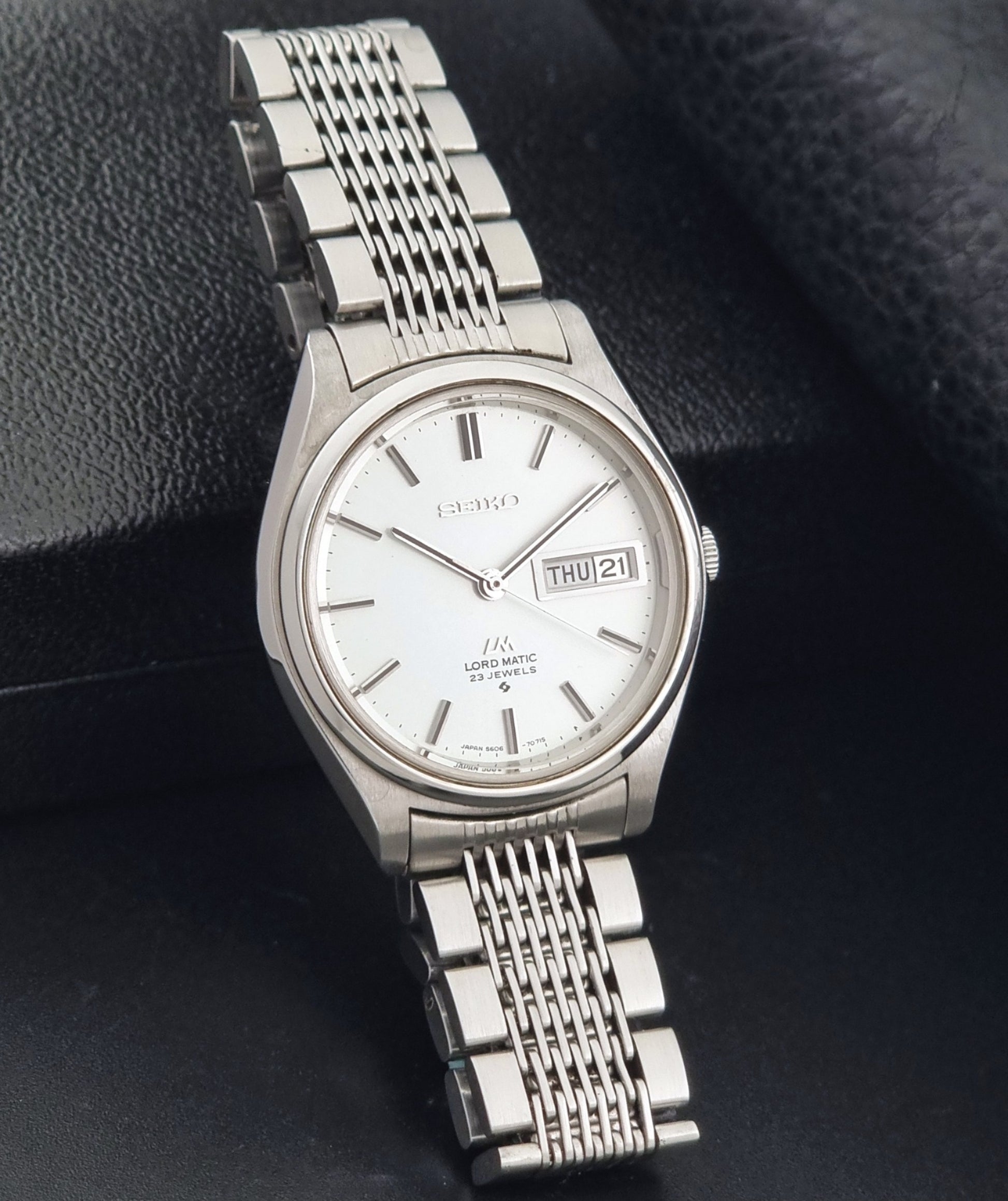 Vintage Seiko 5606-7070 LordMatic with a stainless steel bracelet on a dark background side view