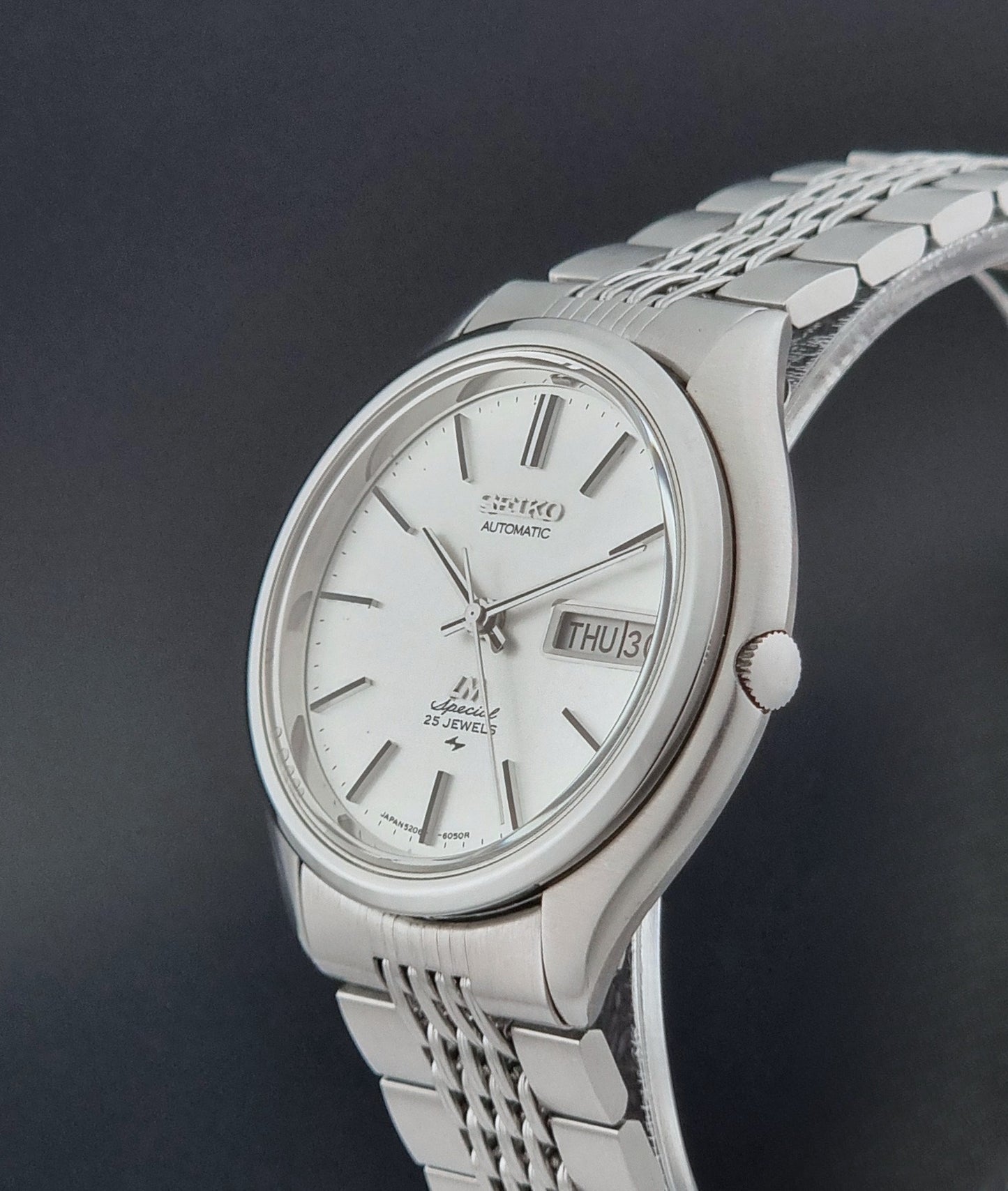 Vintage Seiko watch LordMatic Special 5206-6060 with a white face on a dark gray background crown profile view