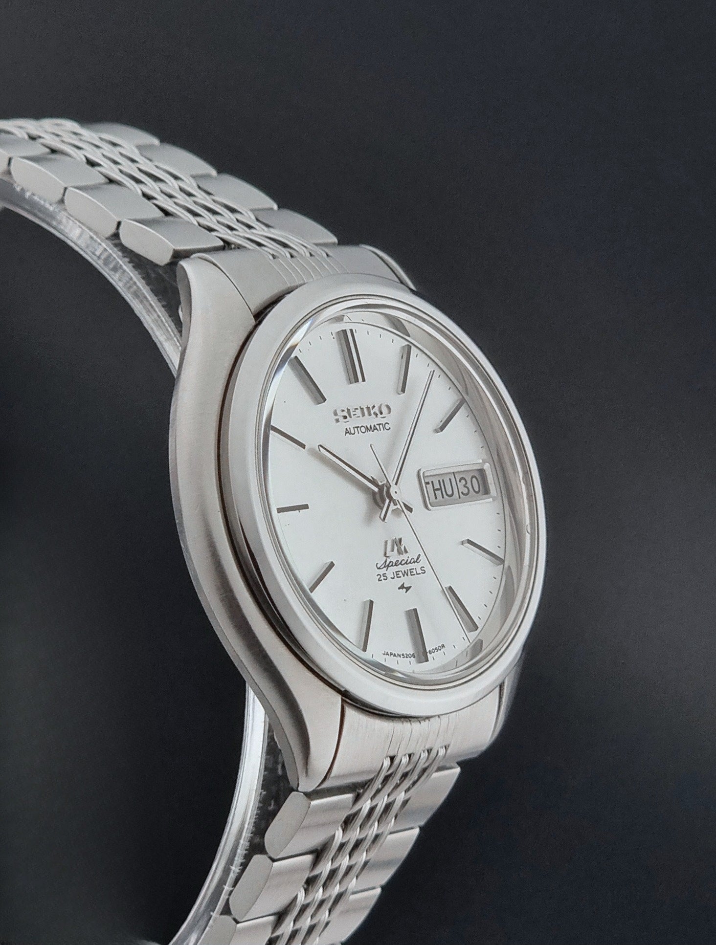 Vintage Seiko watch LordMatic Special 5206-6060 with a white face on a dark gray background side profile view