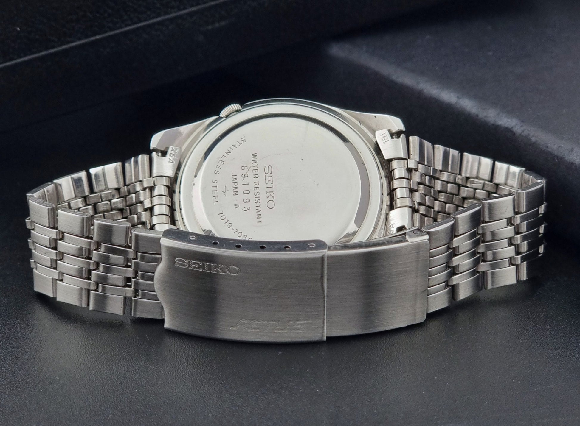 Vintage Seiko 5 Actus Wristwatch 7019-7060 with a stainless steel bracelet on a dark surface case back view