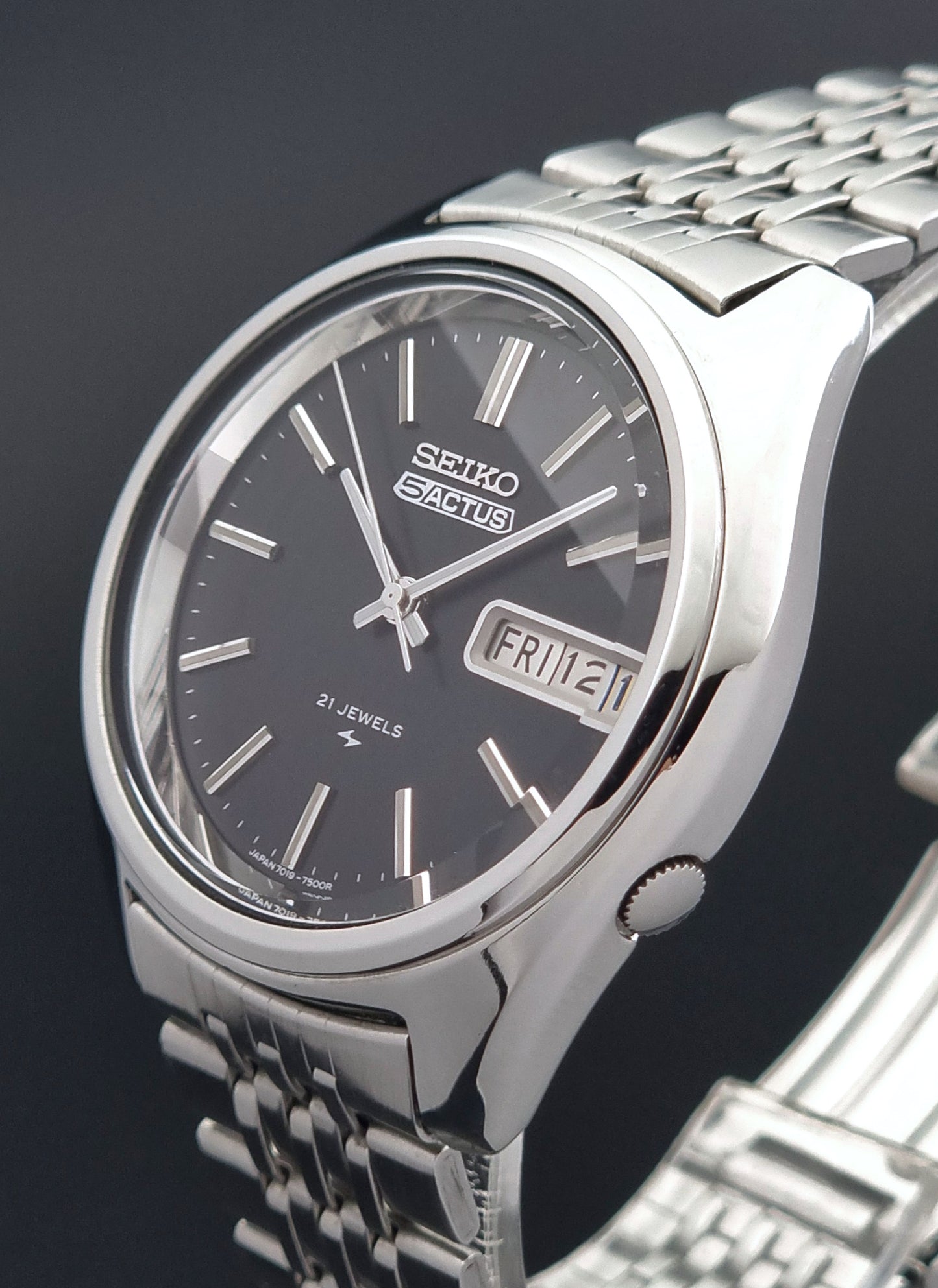 Vintage Seiko 5 Actus Wristwatch 7019-7060 with a stainless steel bracelet on a dark surface crown view