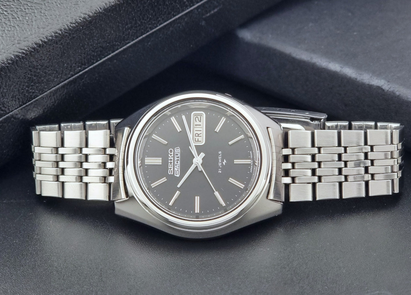 Vintage Seiko 5 Actus Wristwatch 7019-7060 with a stainless steel bracelet on a dark surface front view