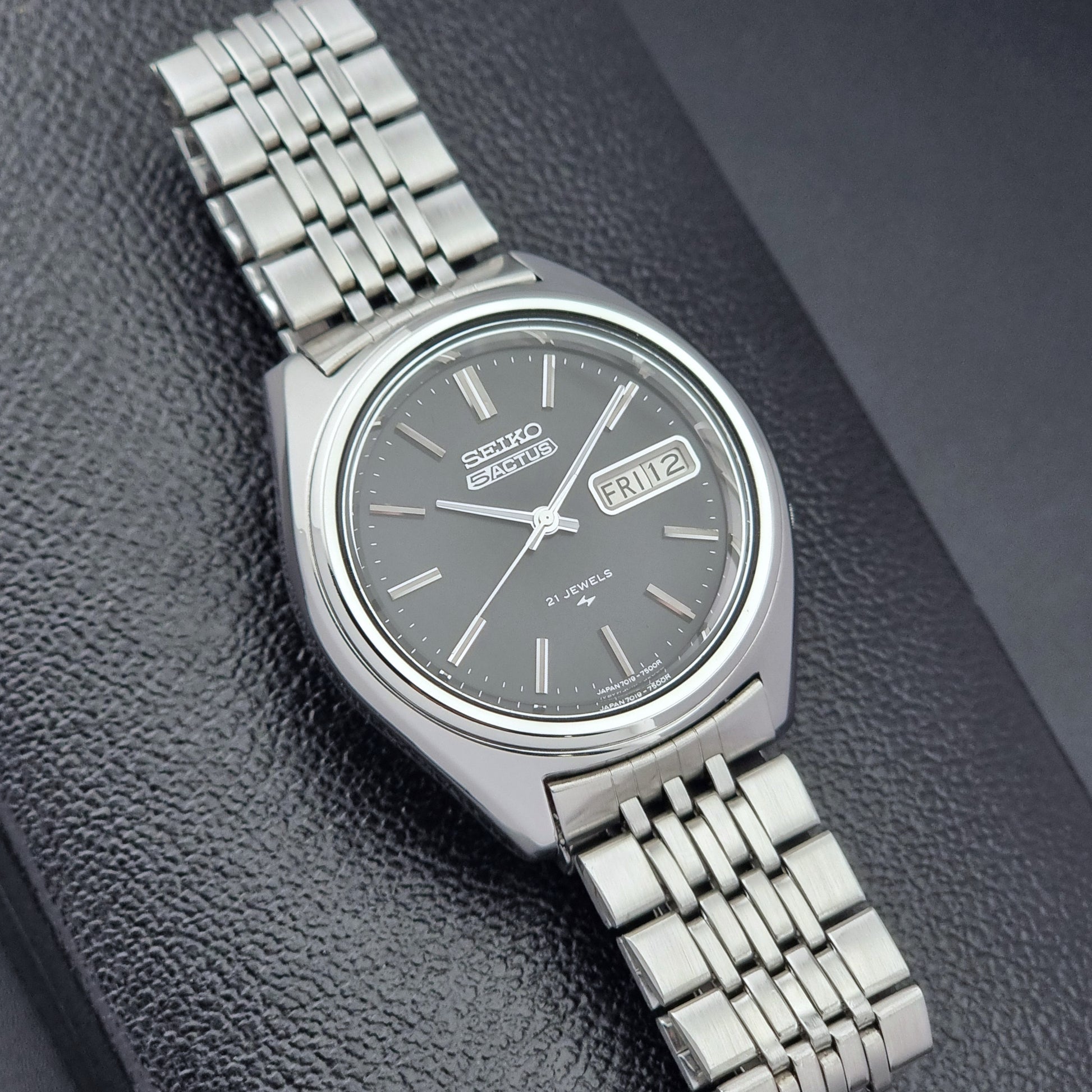 Vintage Seiko 5 Actus Wristwatch 7019-7060 with a stainless steel bracelet on a dark surface close dial view