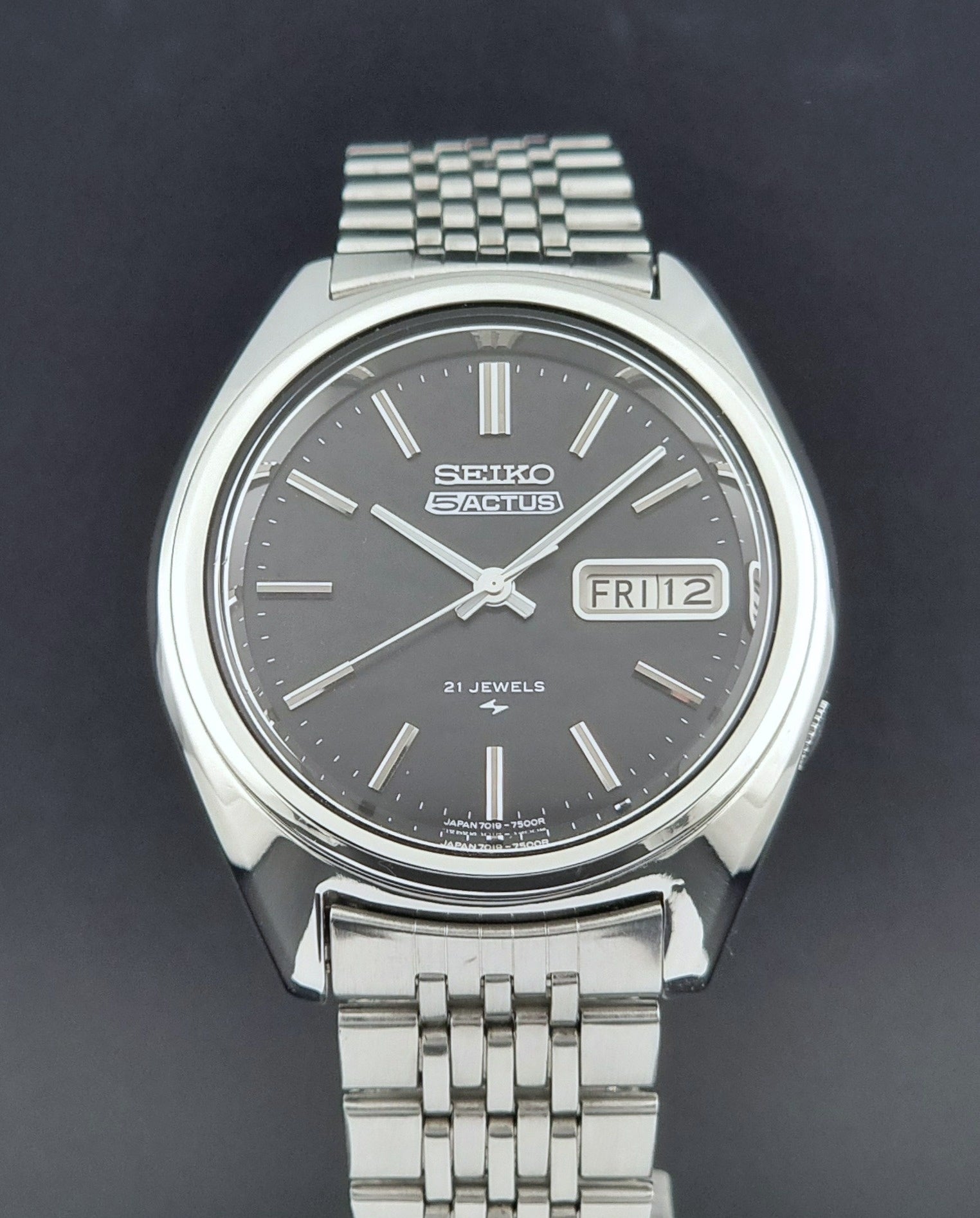 Vintage Seiko 5 Actus Wristwatch 7019-7060 with a stainless steel bracelet on a dark surface dial view