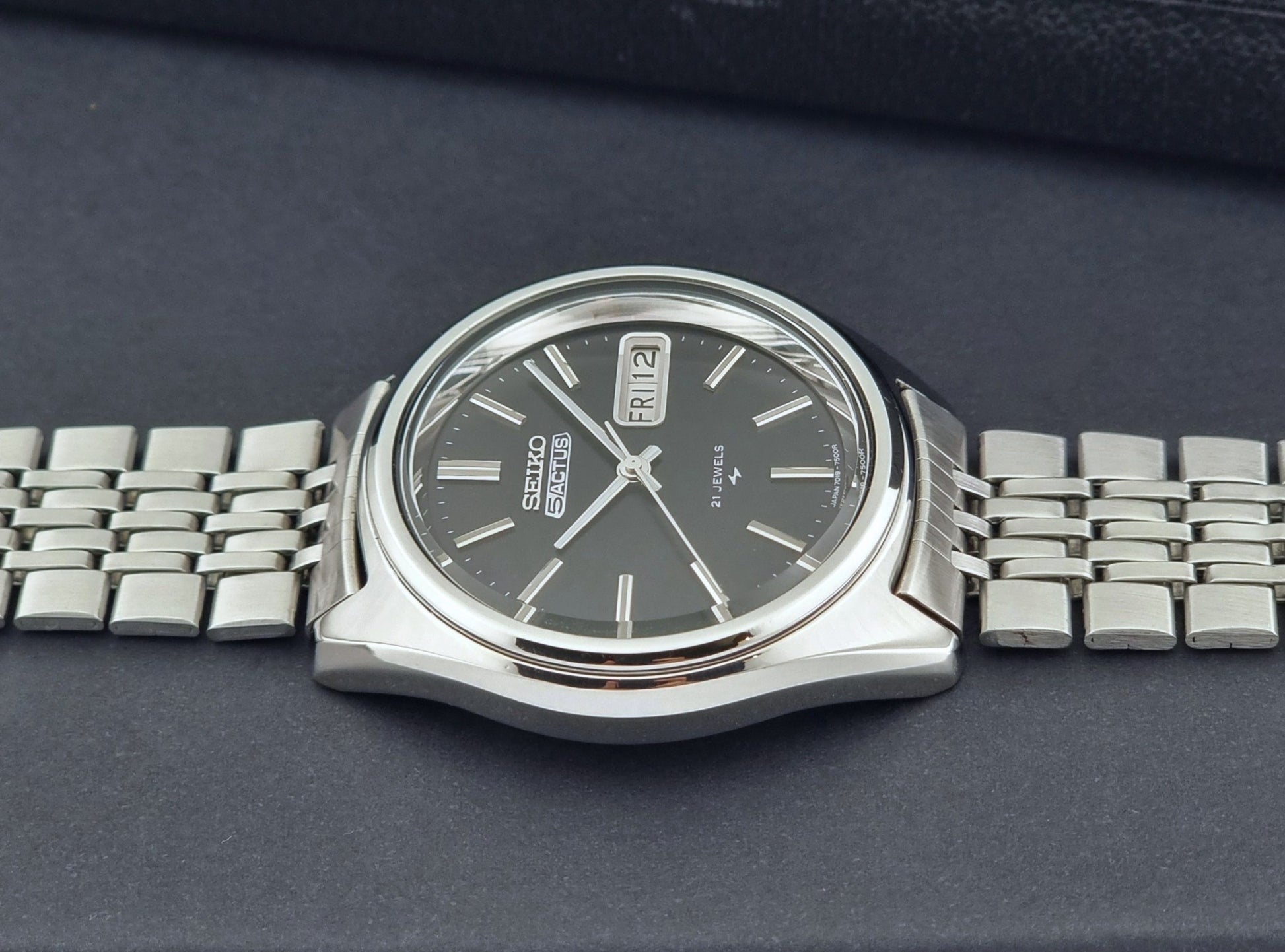 Vintage Seiko 5 Actus Wristwatch 7019-7060 with a stainless steel bracelet on a dark surface side profile view