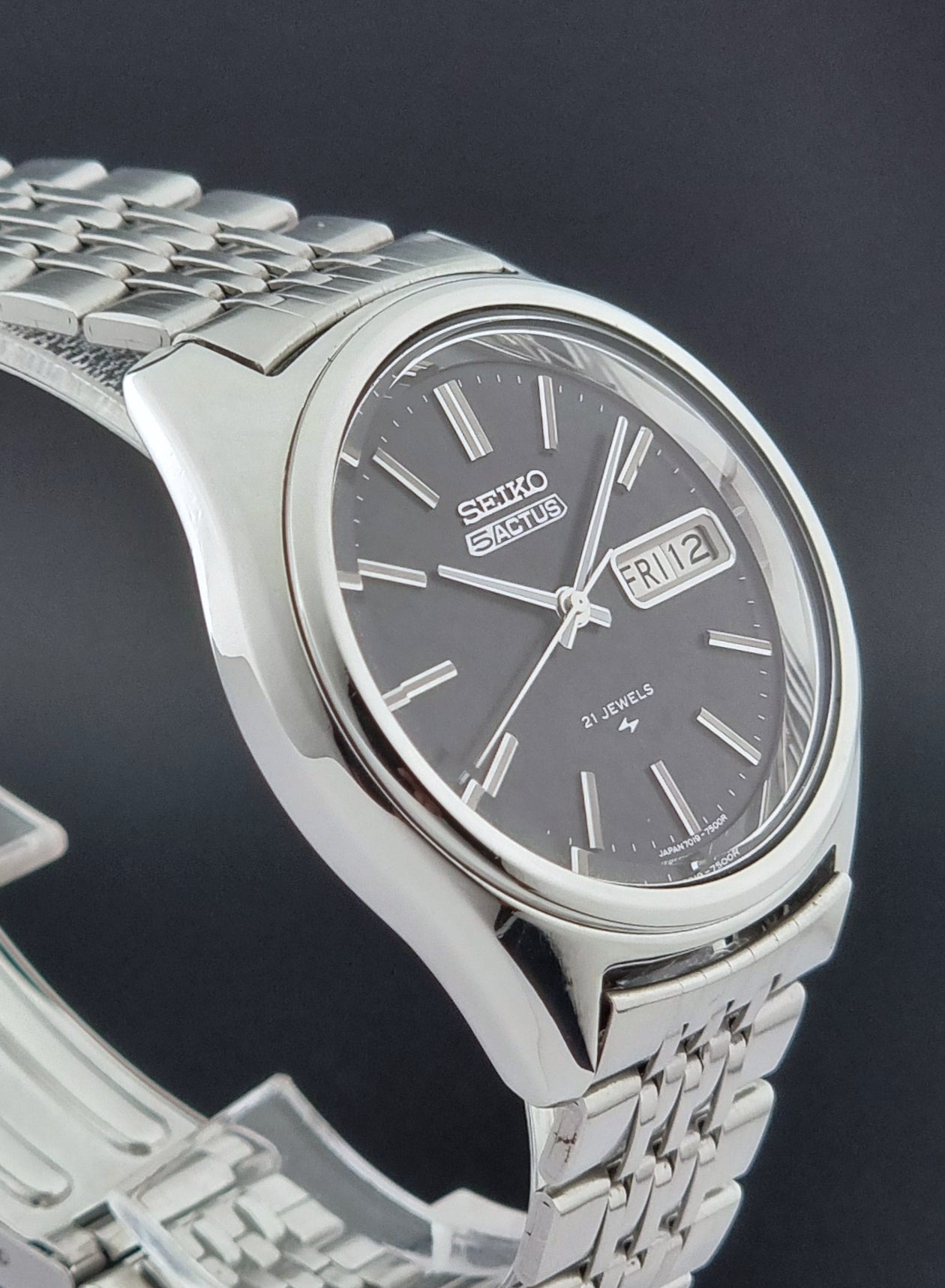 Vintage Seiko 5 Actus Wristwatch 7019-7060 with a stainless steel bracelet on a dark surface side view