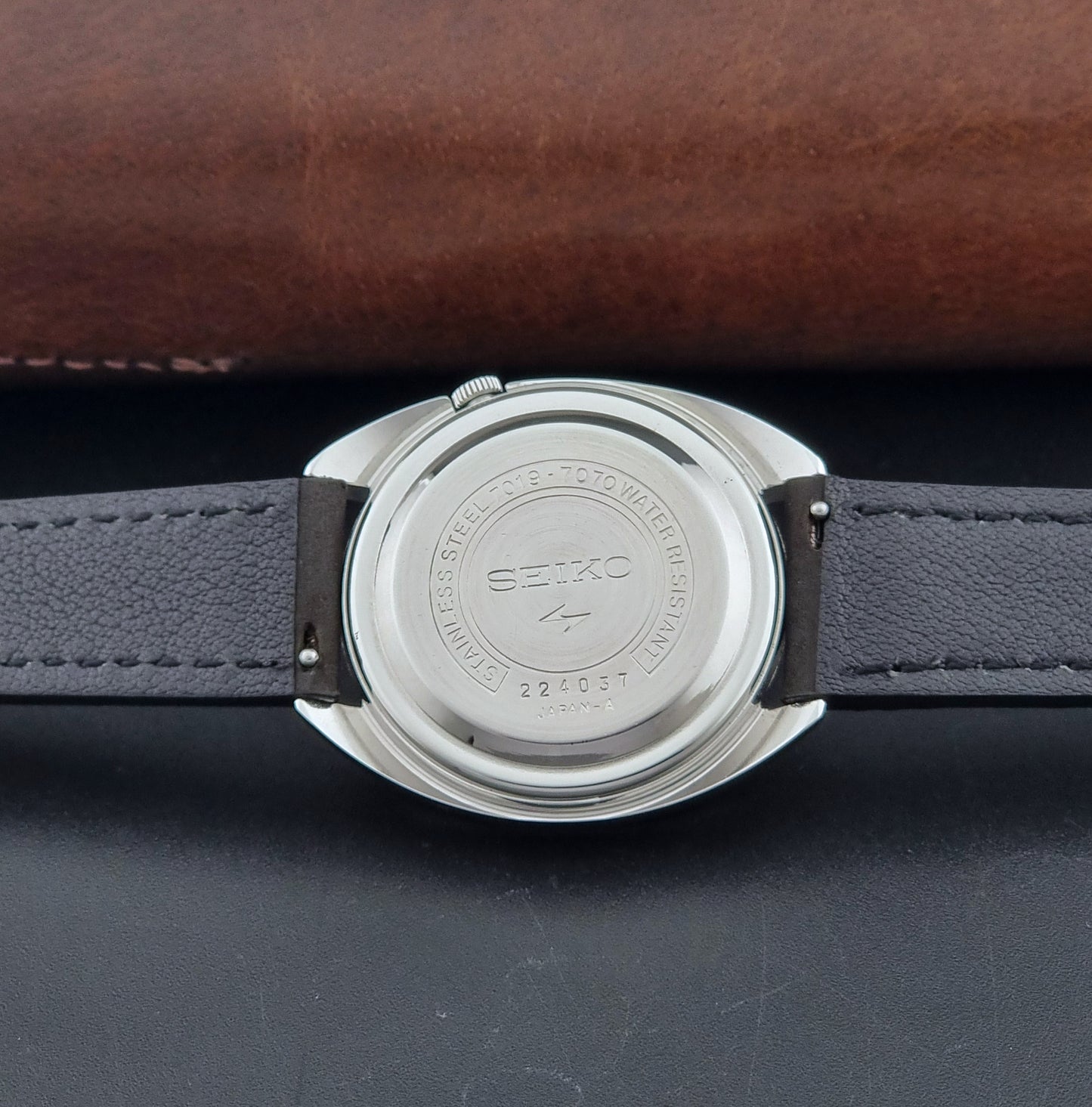 Vintage Seiko 5 Actus Wristwatch 7019-7070 watch with a dark leather strap on a gray surface case back view