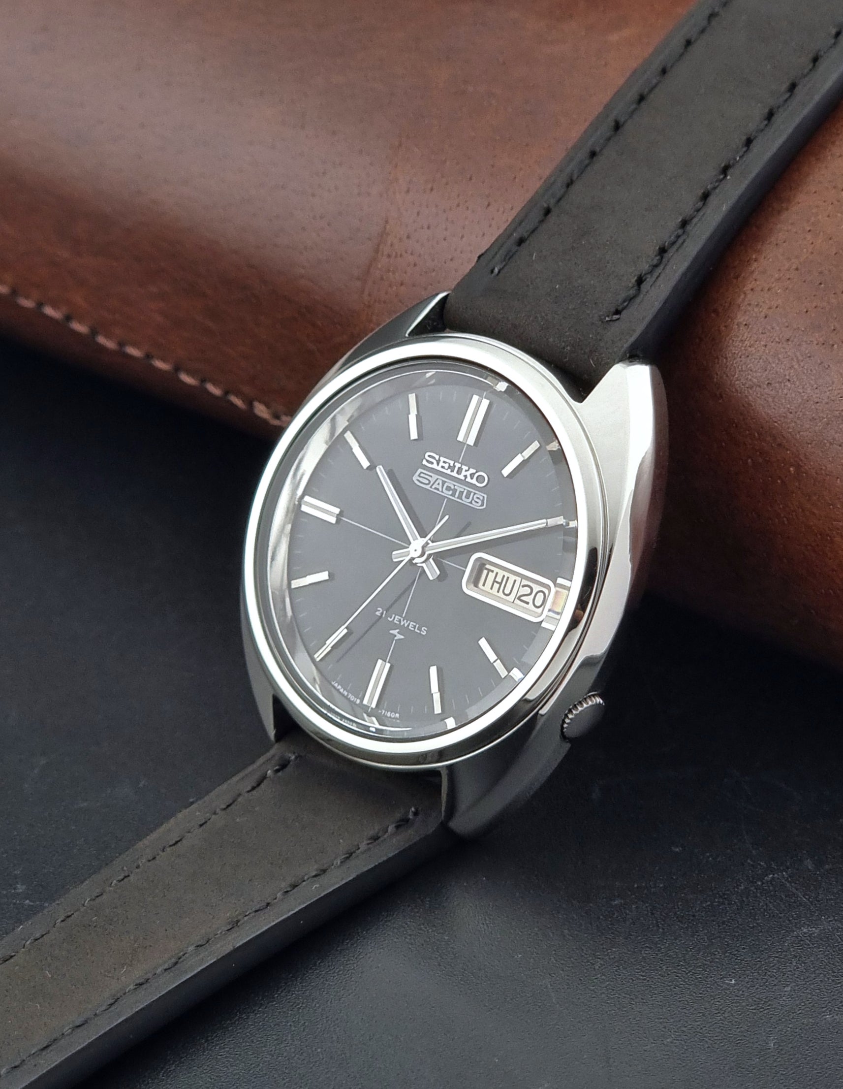 Vintage Seiko 5 Actus Wristwatch 7019-7070 watch with a dark leather strap on a gray surface crown view