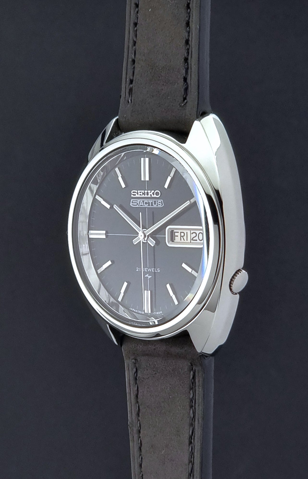 Vintage Seiko 5 Actus Wristwatch 7019-7070 watch with a dark leather strap on a gray surface crown profile view