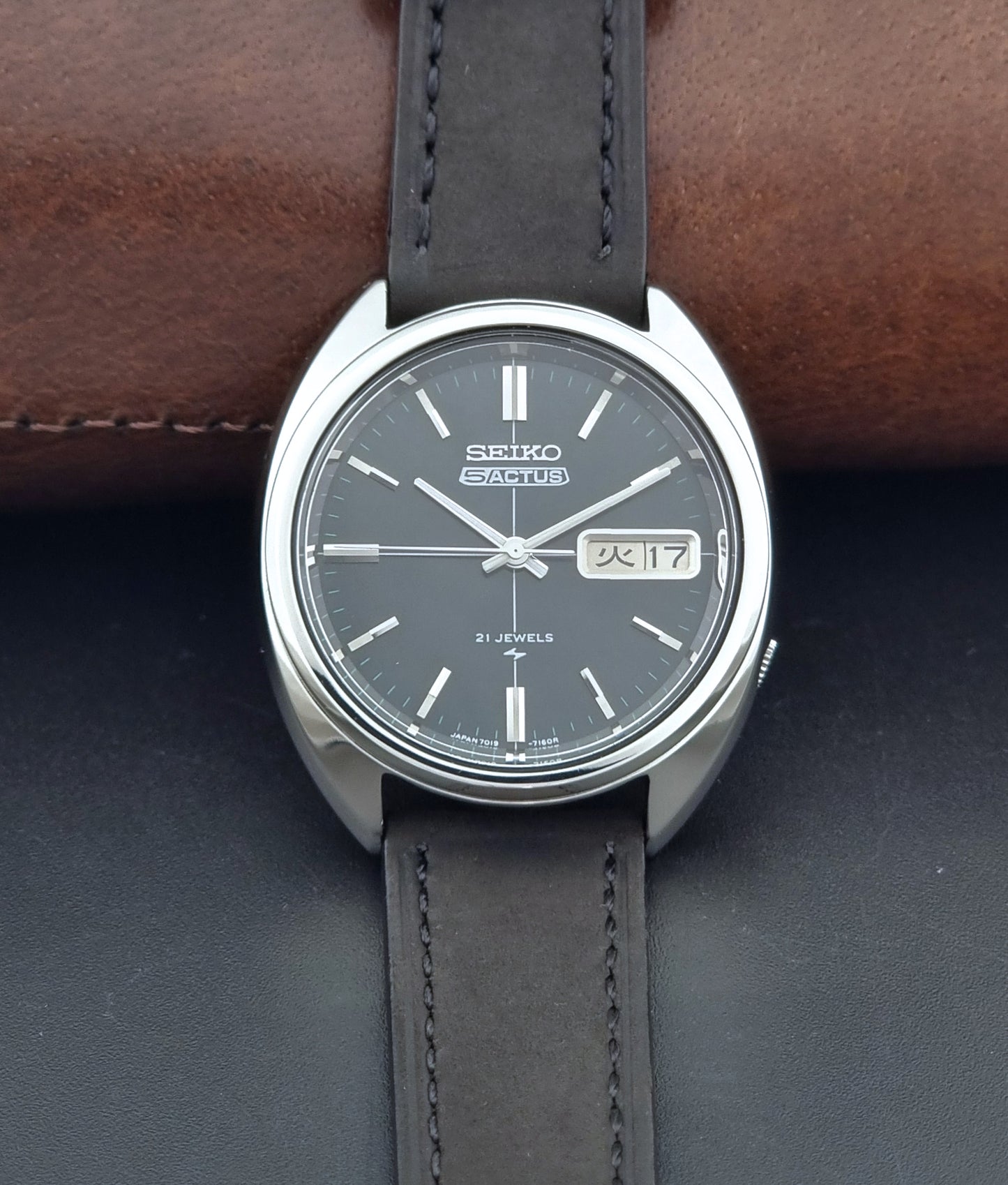 Vintage Seiko 5 Actus Wristwatch 7019-7070 watch with a dark leather strap on a gray surface dial view