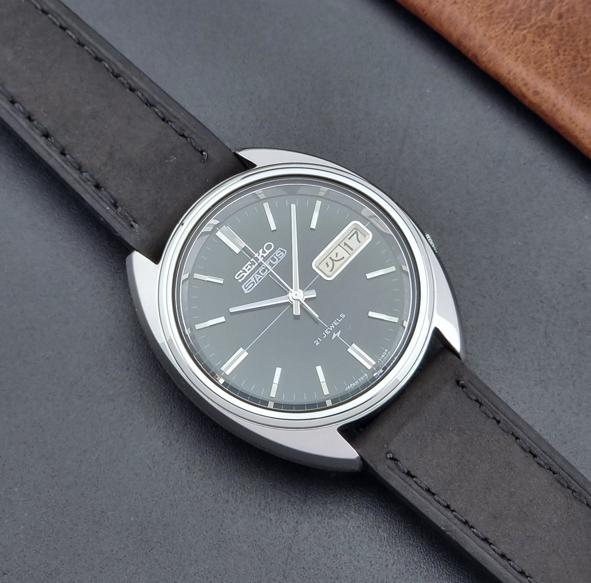 Vintage Seiko 5 Actus Wristwatch 7019-7070 watch with a dark leather strap on a gray surface close up dial view