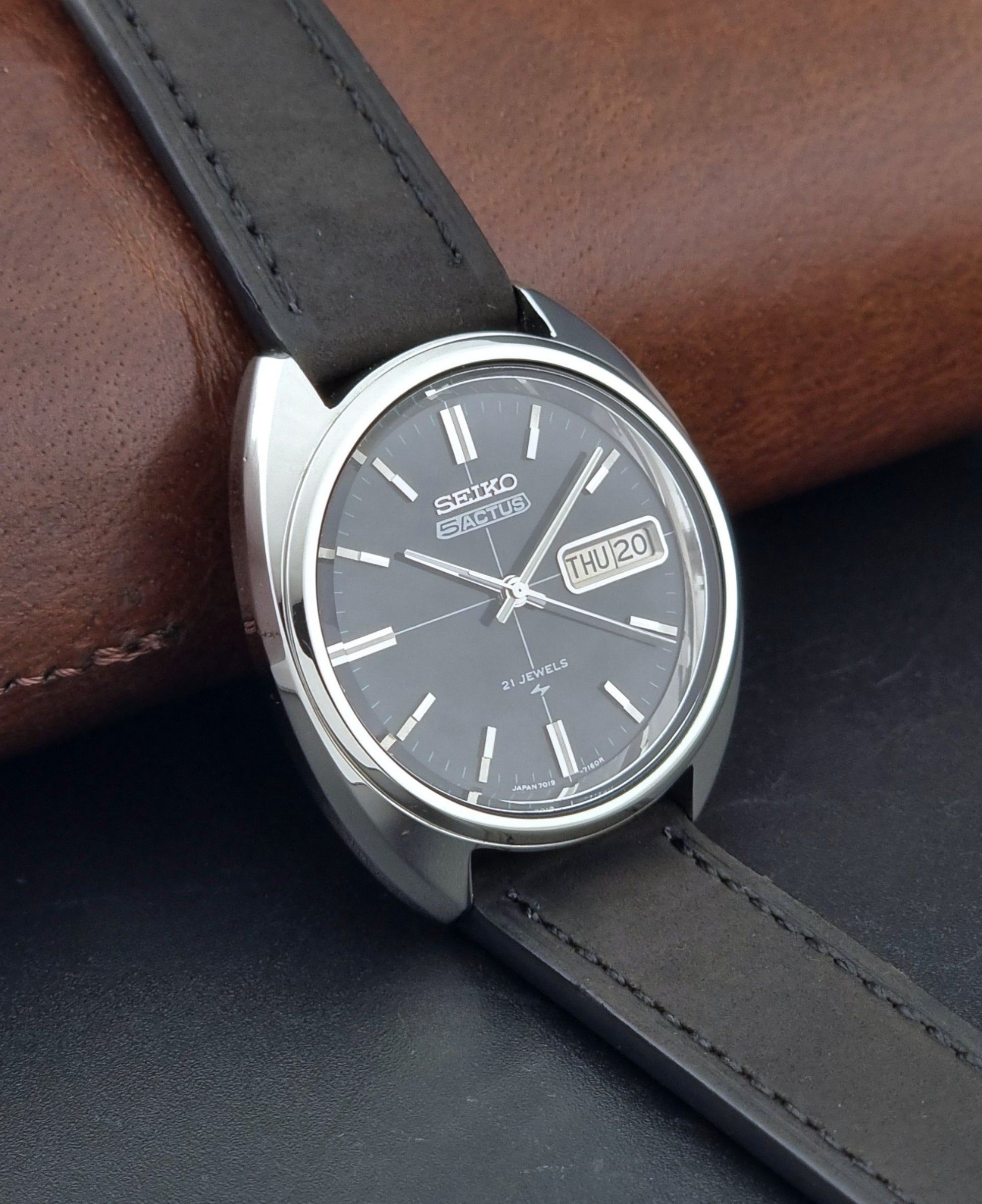Vintage Seiko 5 Actus Wristwatch 7019-7070 watch with a dark leather strap on a gray surface side view