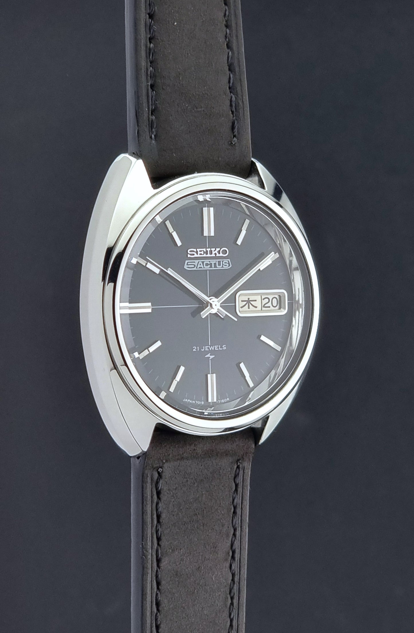 Vintage Seiko 5 Actus Wristwatch 7019-7070 watch with a dark leather strap on a gray surface side profile view