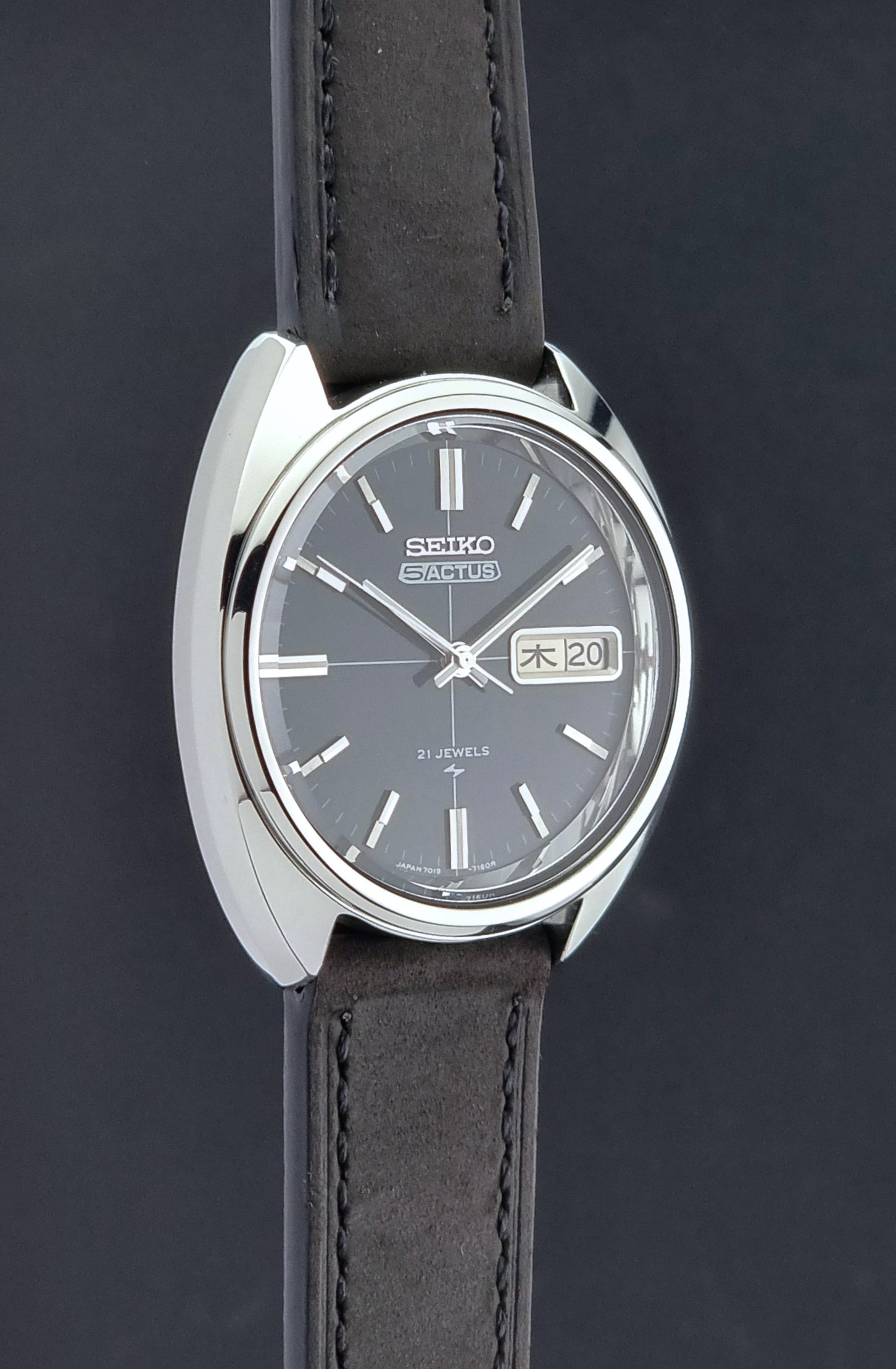 Vintage Seiko 5 Actus Wristwatch 7019-7070 watch with a dark leather strap on a gray surface side profile view