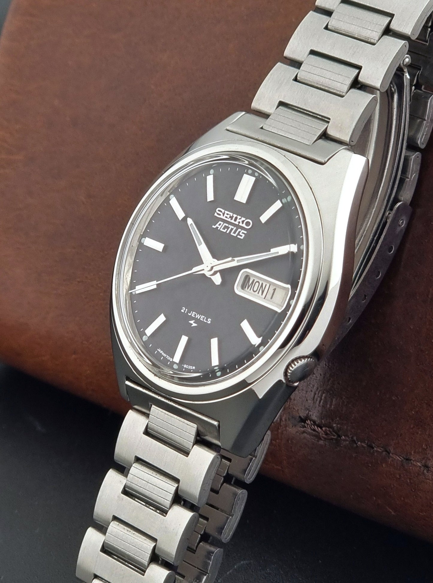 Vintage Seiko Actus Wristwatch 7019-8010 with a Black dial and bracelet on a dark back ground crown view