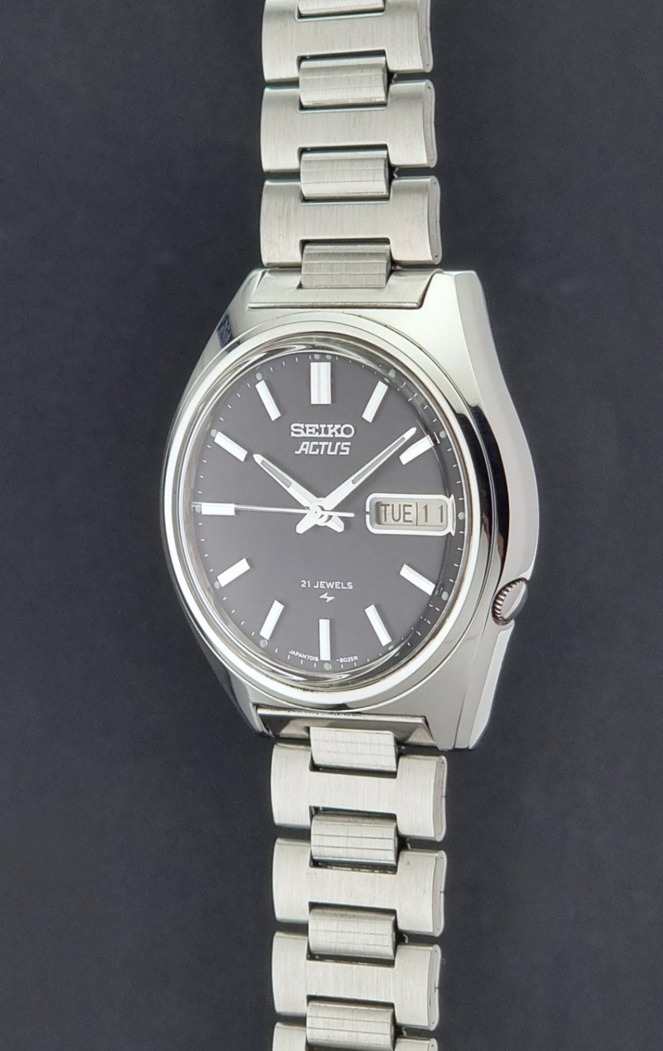 Vintage Seiko Actus Wristwatch 7019-8010 with a Black dial and bracelet on a dark back ground crown profile view