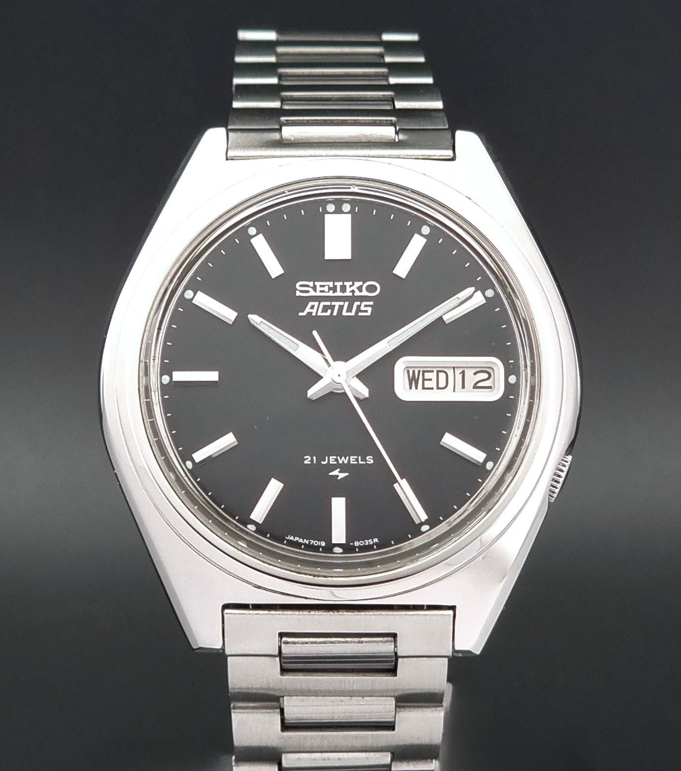 Vintage Seiko Actus Wristwatch 7019-8010 with a Black dial and bracelet on a dark back ground close dial view