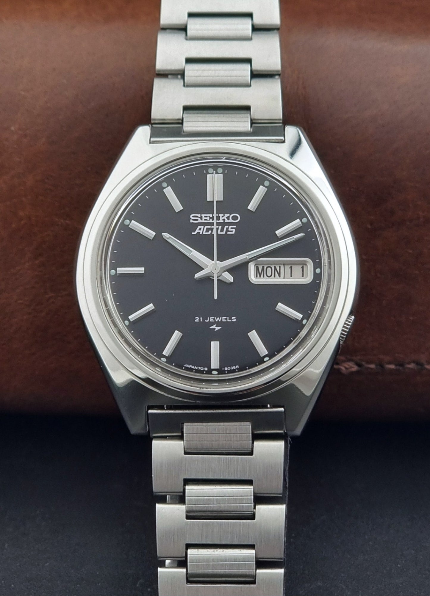 Vintage Seiko Actus Wristwatch 7019-8010 with a Black dial and bracelet on a dark back ground dial view
