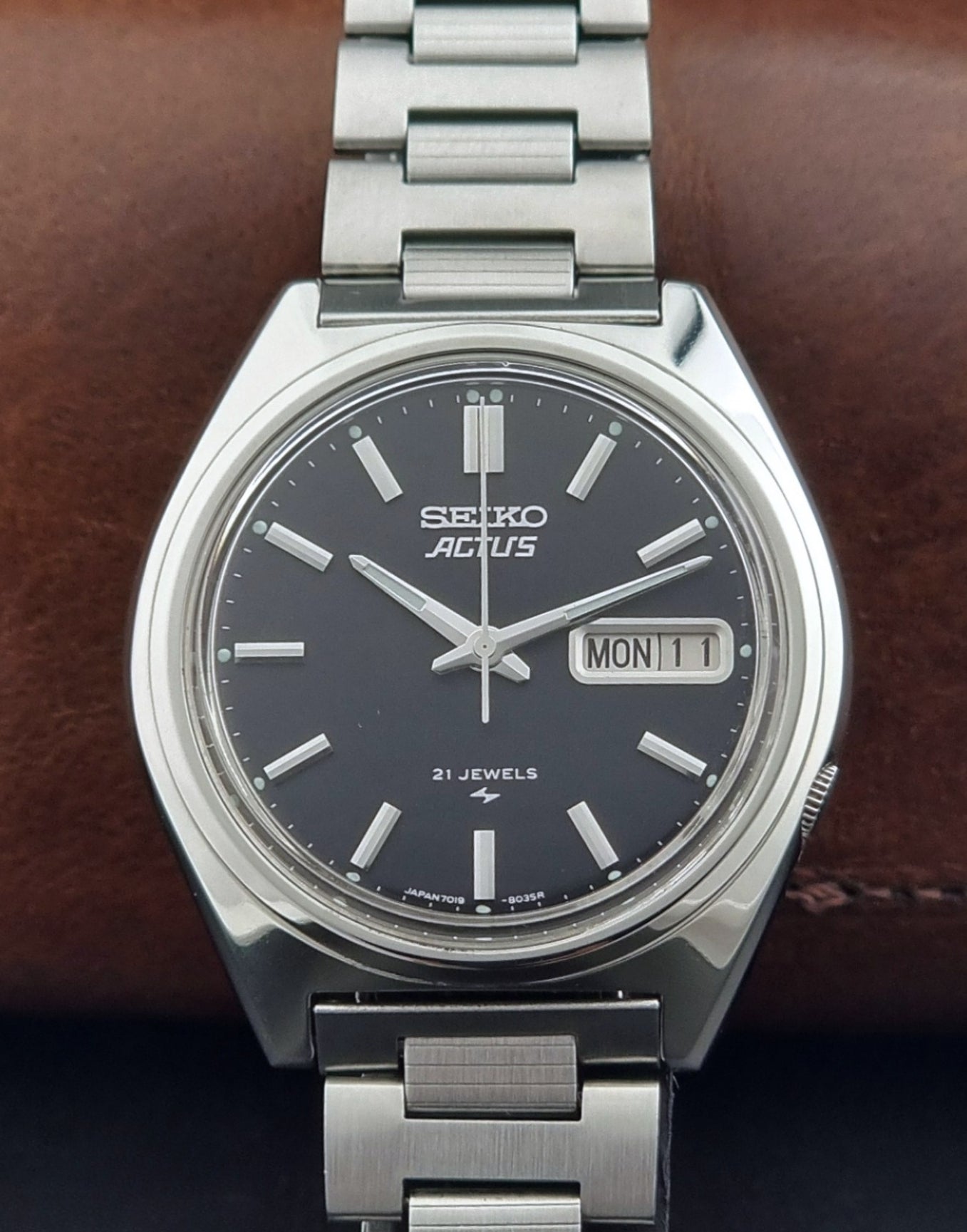 Vintage Seiko Actus Wristwatch 7019-8010 with a Black dial and bracelet on a dark back ground front view